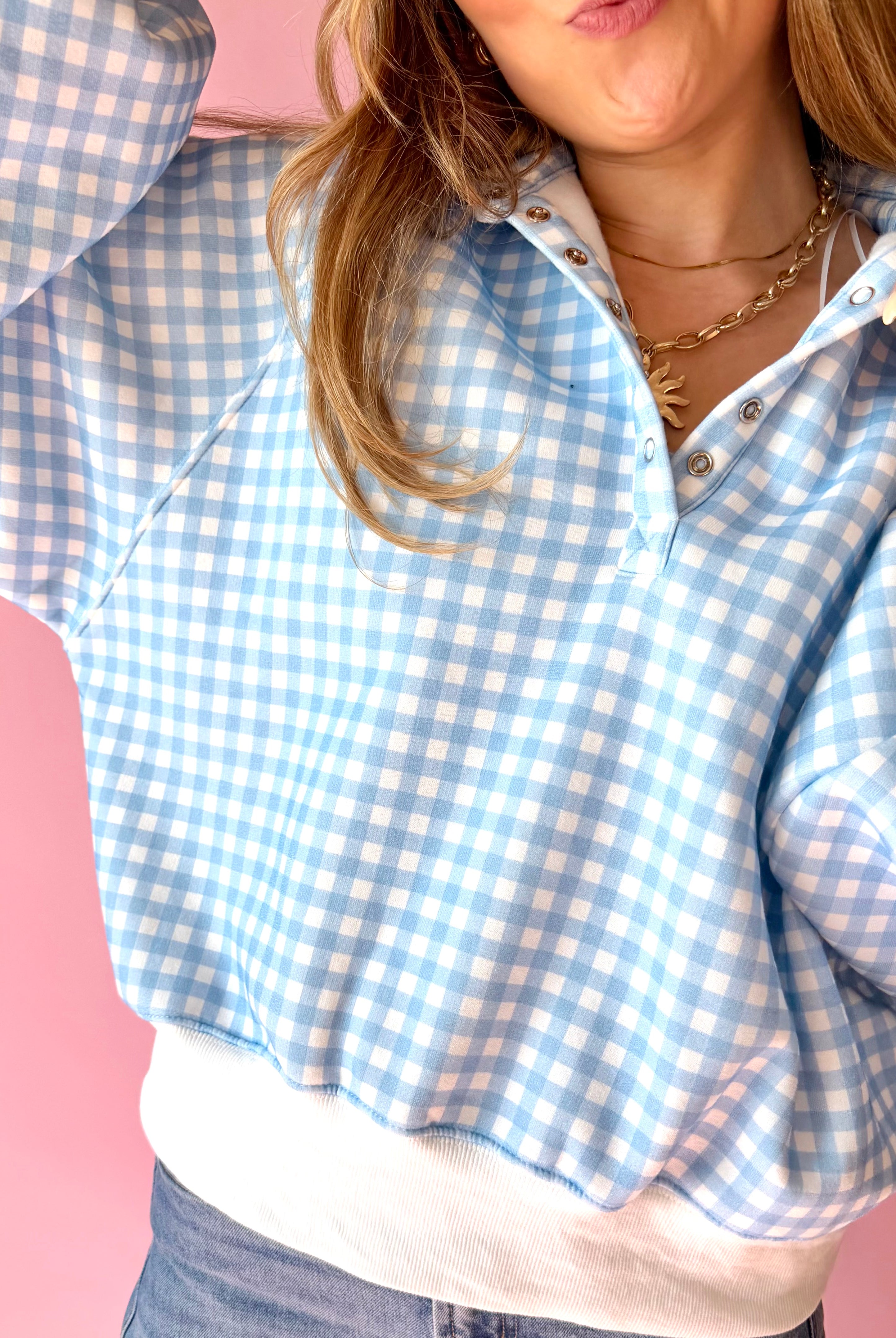 Person wearing a blue and white checkered shirt against a pink background, blue and white, gingham, blue picnic, quarter snap, over-sized, comfy pullover, lounge wear