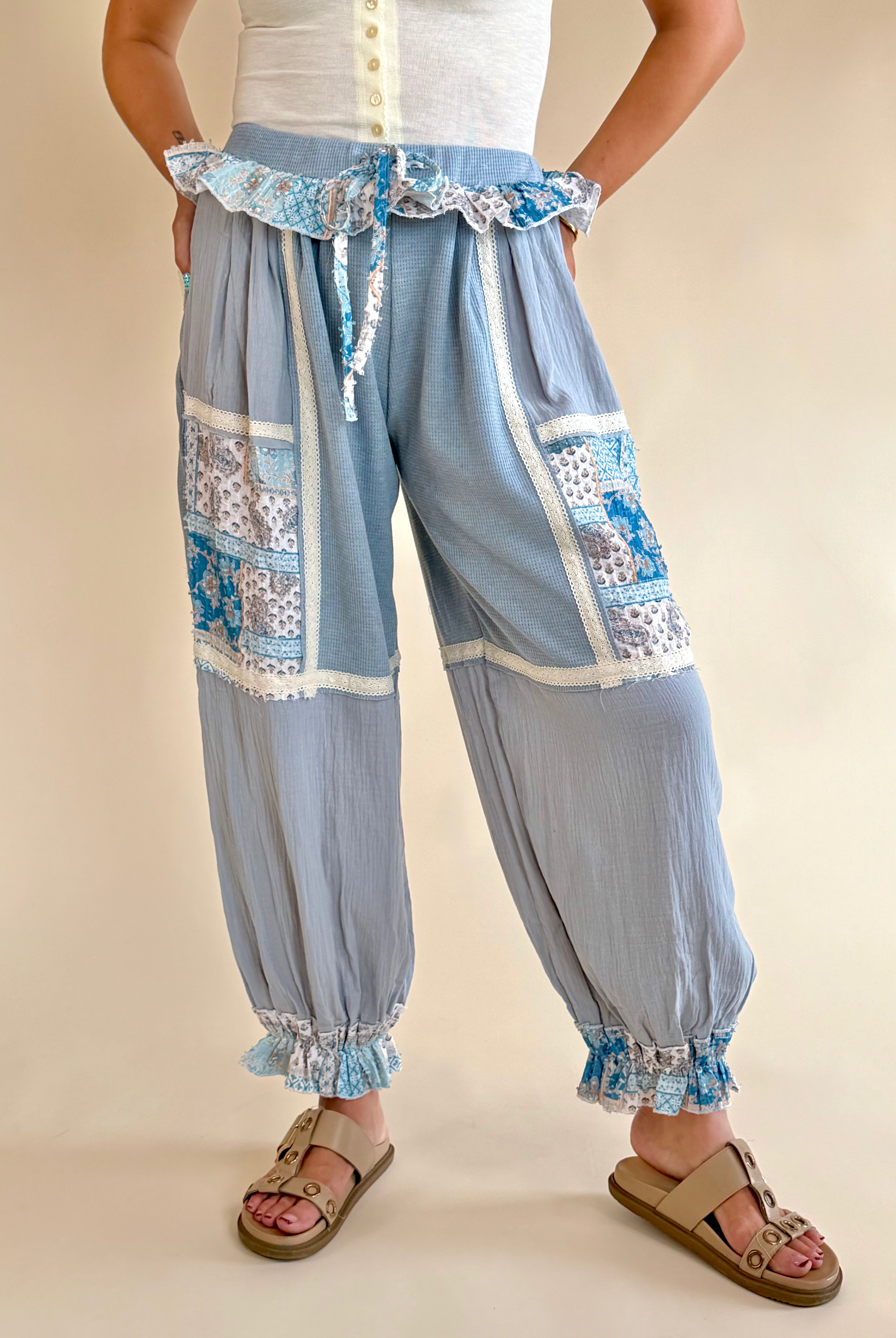 Light blue patchwork pants with decorative ruffles on a beige background, bandana print patchwork, shades of blue, white trim detail, ruffle waist sweatpant, synched bottom pant