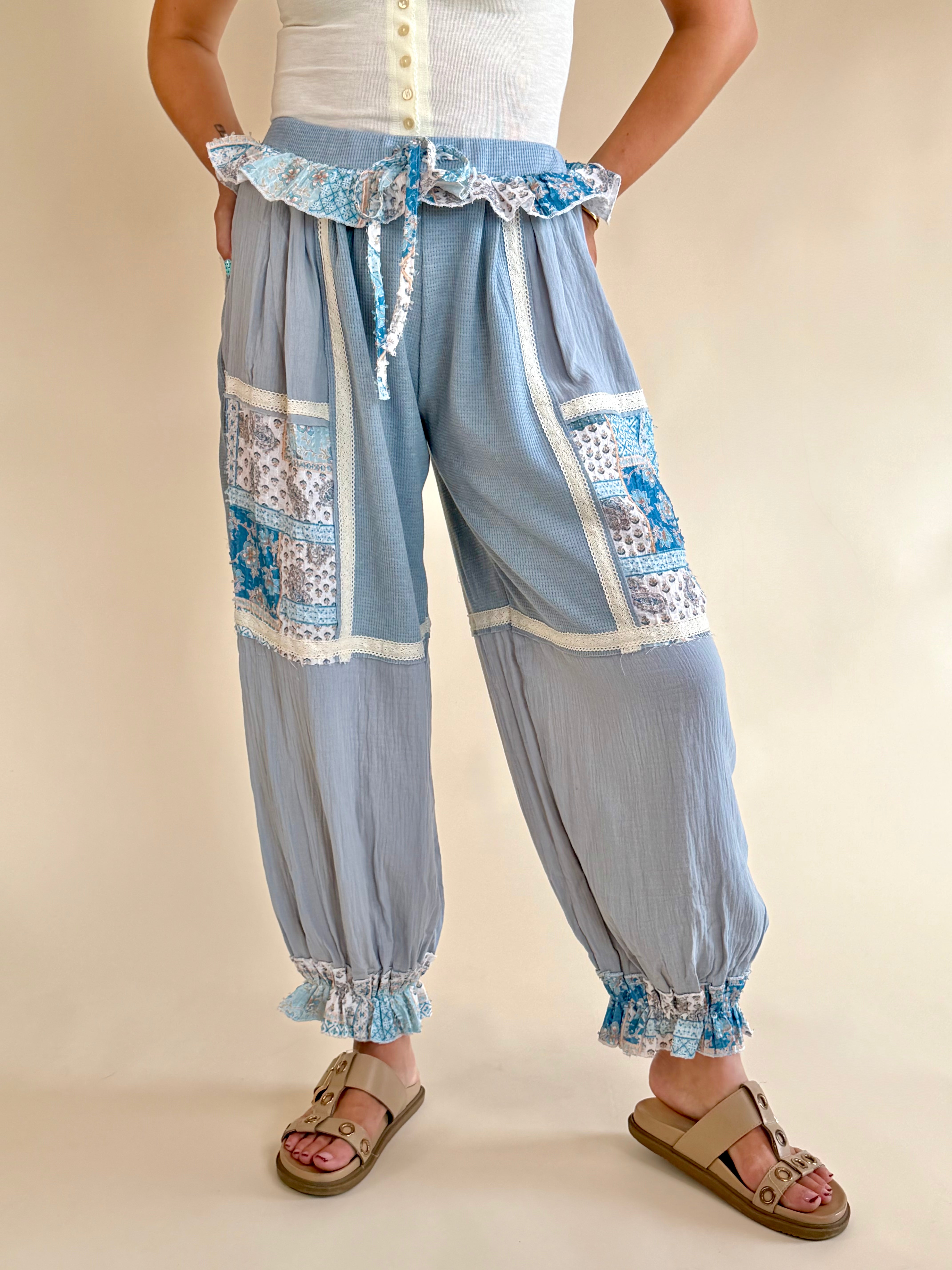 Light blue patchwork pants with decorative ruffles on a beige background, bandana print patchwork, shades of blue, white trim detail, ruffle waist sweatpant, synched bottom pant