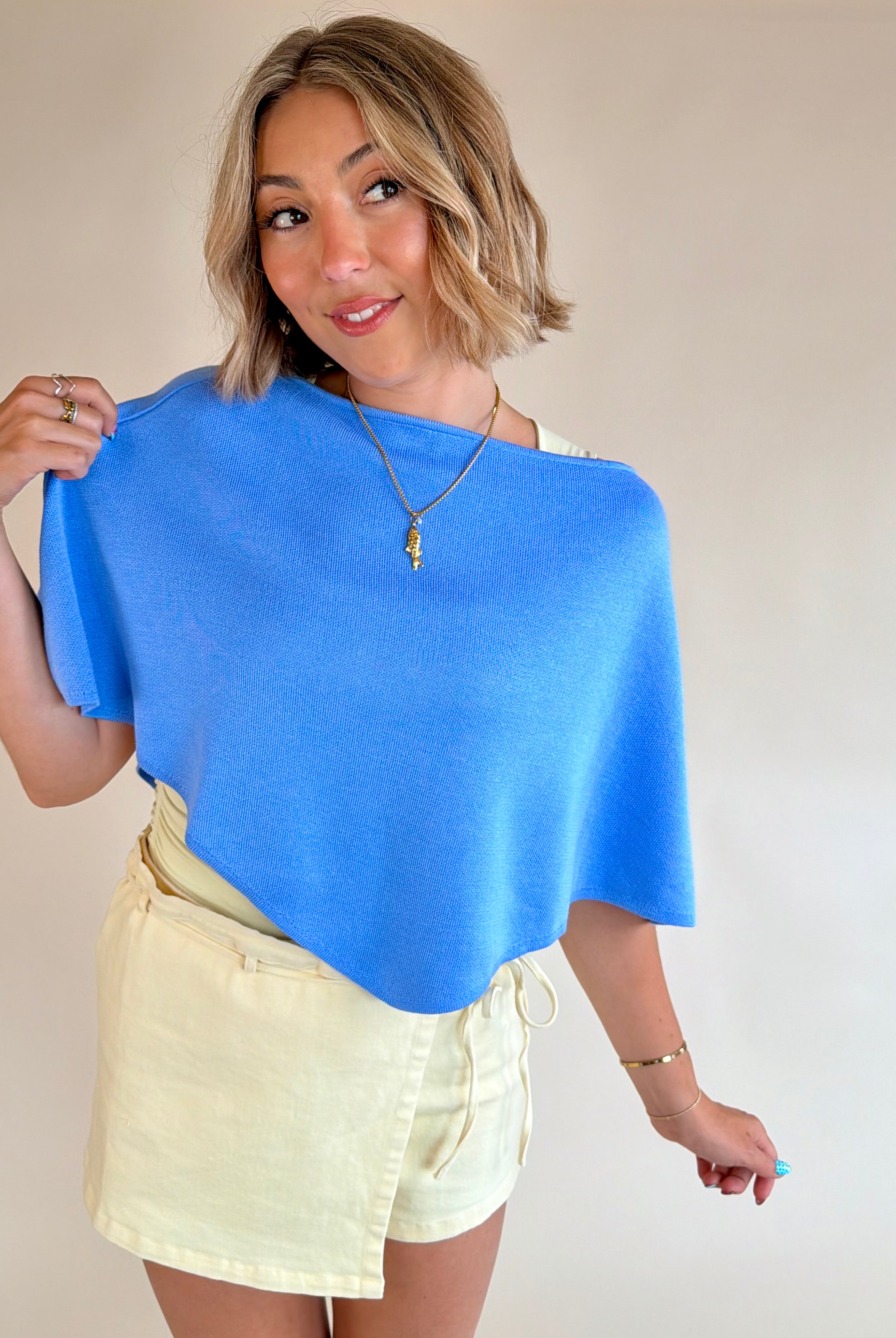 Woman wearing a blue top and yellow skirt against a plain background, Blue poncho top, summer staple, ocean blue, style piece, flattering fit
