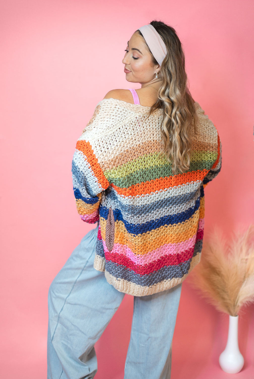 Back view with blue jeans: Cream Rainbow Cardigan with multicolor stripes, an open front, and hip pockets.