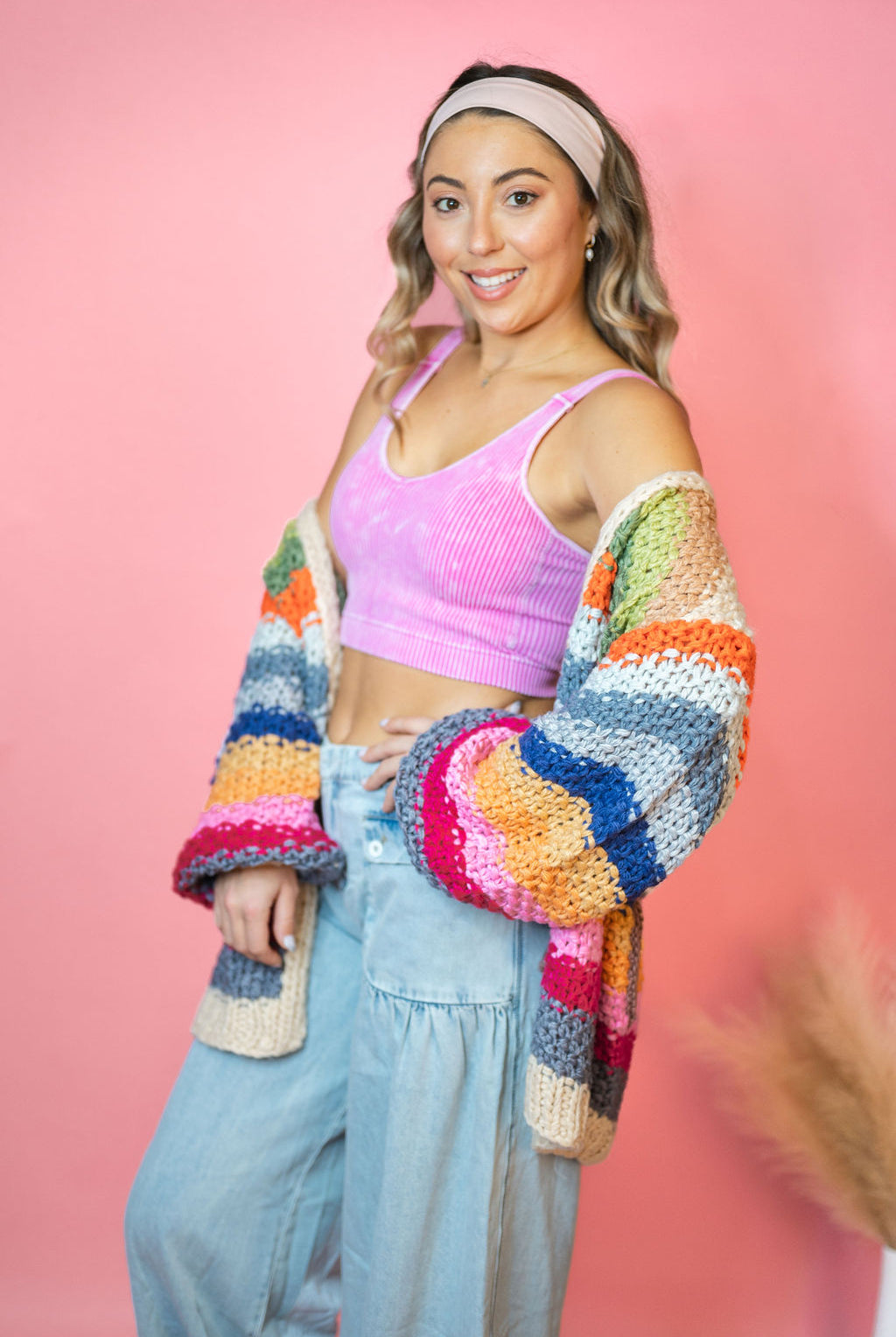 Front view with pink top and blue jeans: Cream Rainbow Cardigan with multicolor stripes, an open front, and hip pockets.