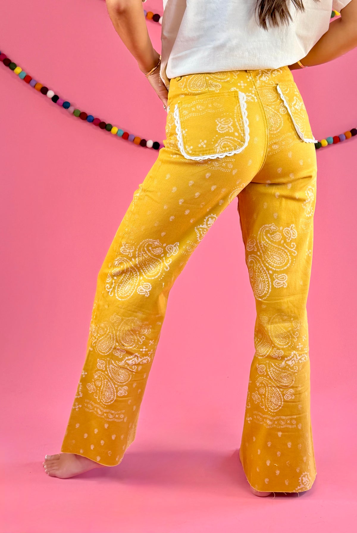 Side and back fit view: POPPY & PINE mustard yellow bandana paisley denim pants with frayed hems.