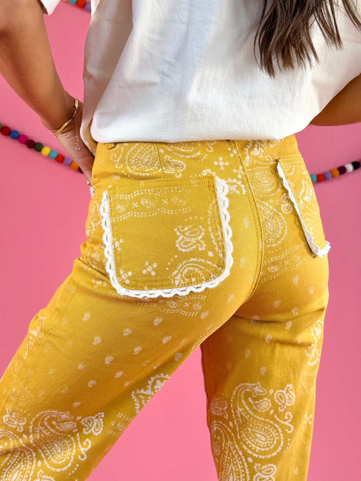 Rear pocket close-up: POPPY & PINE mustard yellow bandana paisley denim pants with frayed hems.