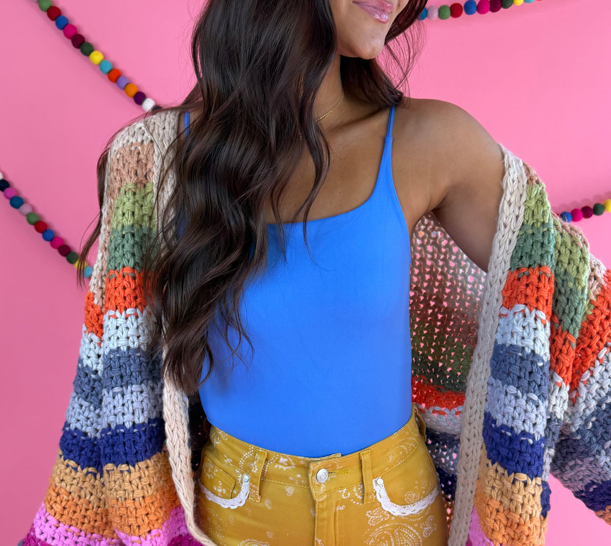Styled with blue tank and mustard pants: Cream Rainbow Cardigan with multicolor stripes, an open front, and hip pockets.