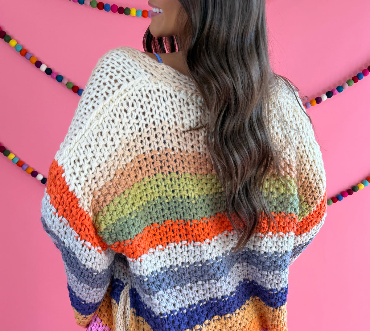 Back view: Cream Rainbow Cardigan with multicolor stripes, an open front, and hip pockets.