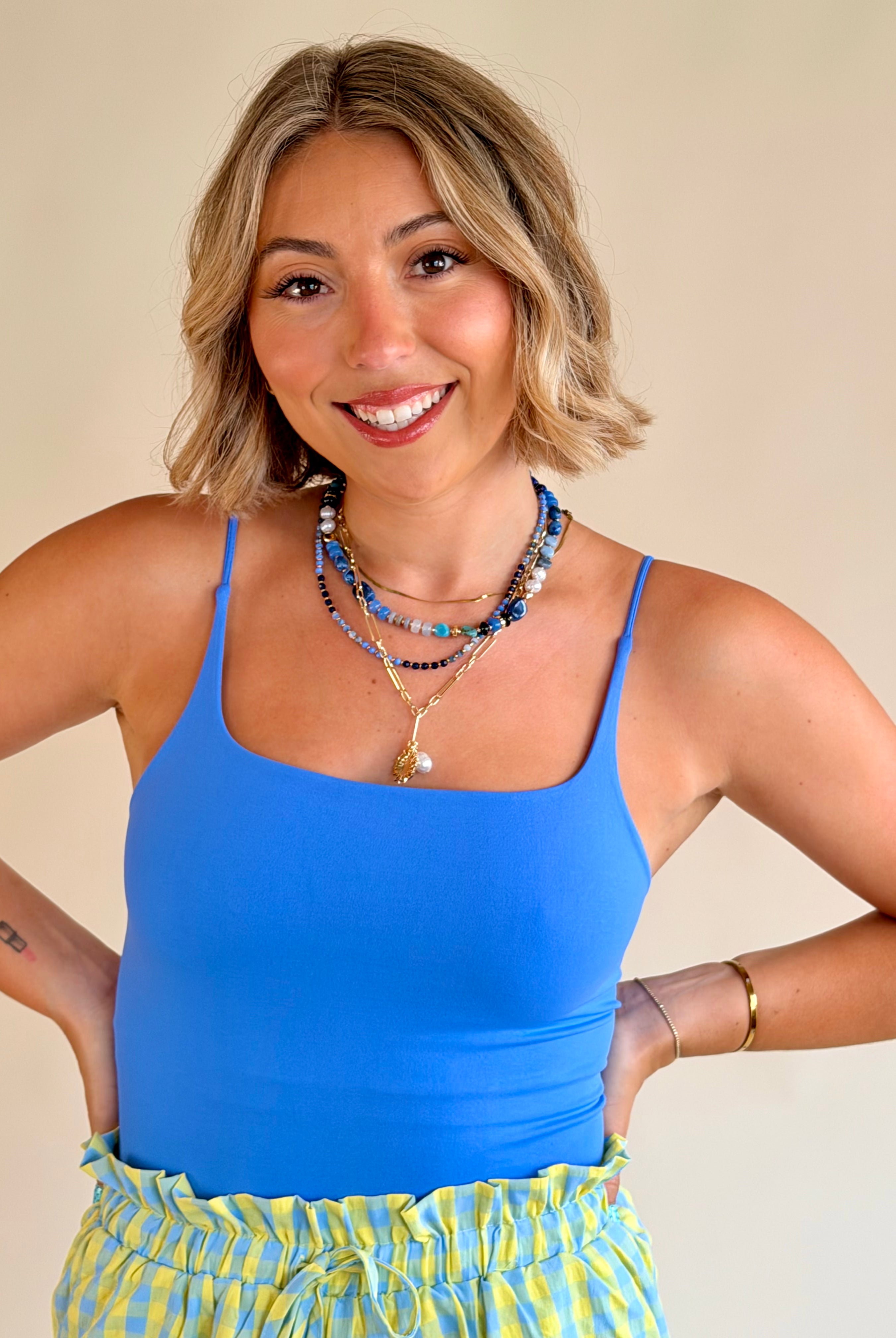 Woman wearing a blue tank top and yellow plaid shorts with a beige background, everyday basic, blue tank, flattering fit, marina blue
