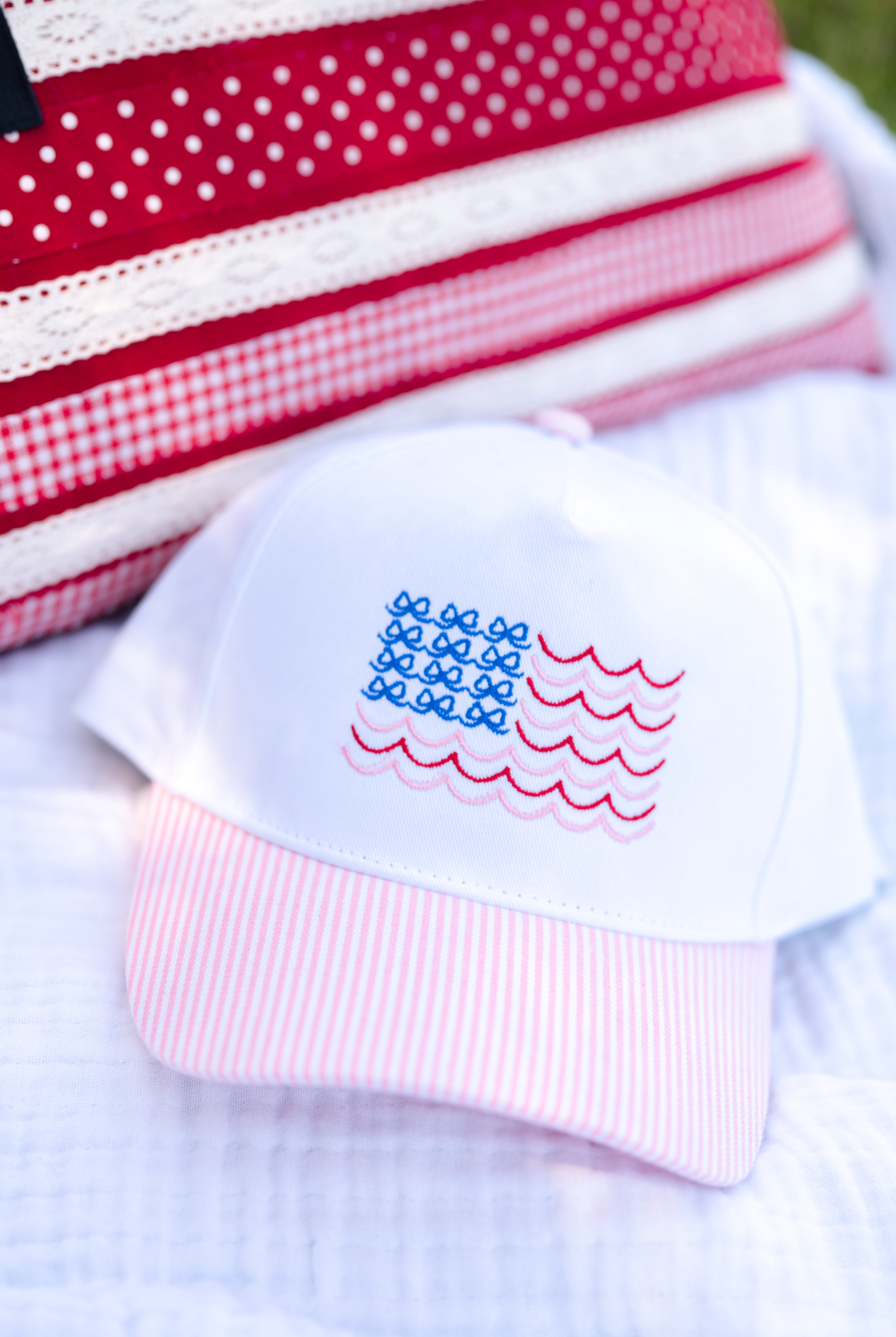 White baby hat with American flag design on a white blanket, pink and white, bows and stripes, beachy and bows, USA