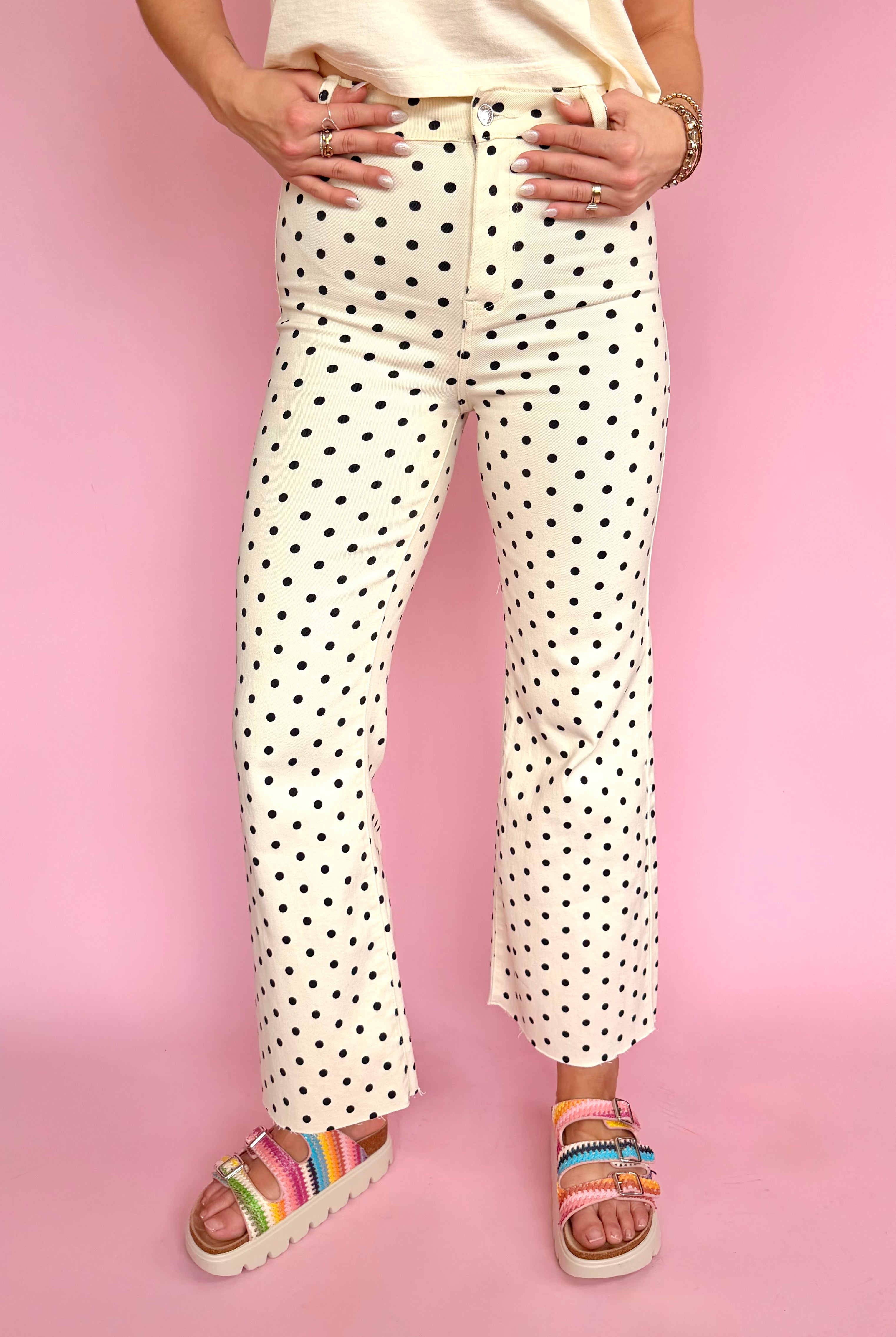 Person wearing polka dot pants and colorful sandals on a pink background, polka dot flare pant, raw hem bottom, high waisted jean, stretchy comfy summer pant