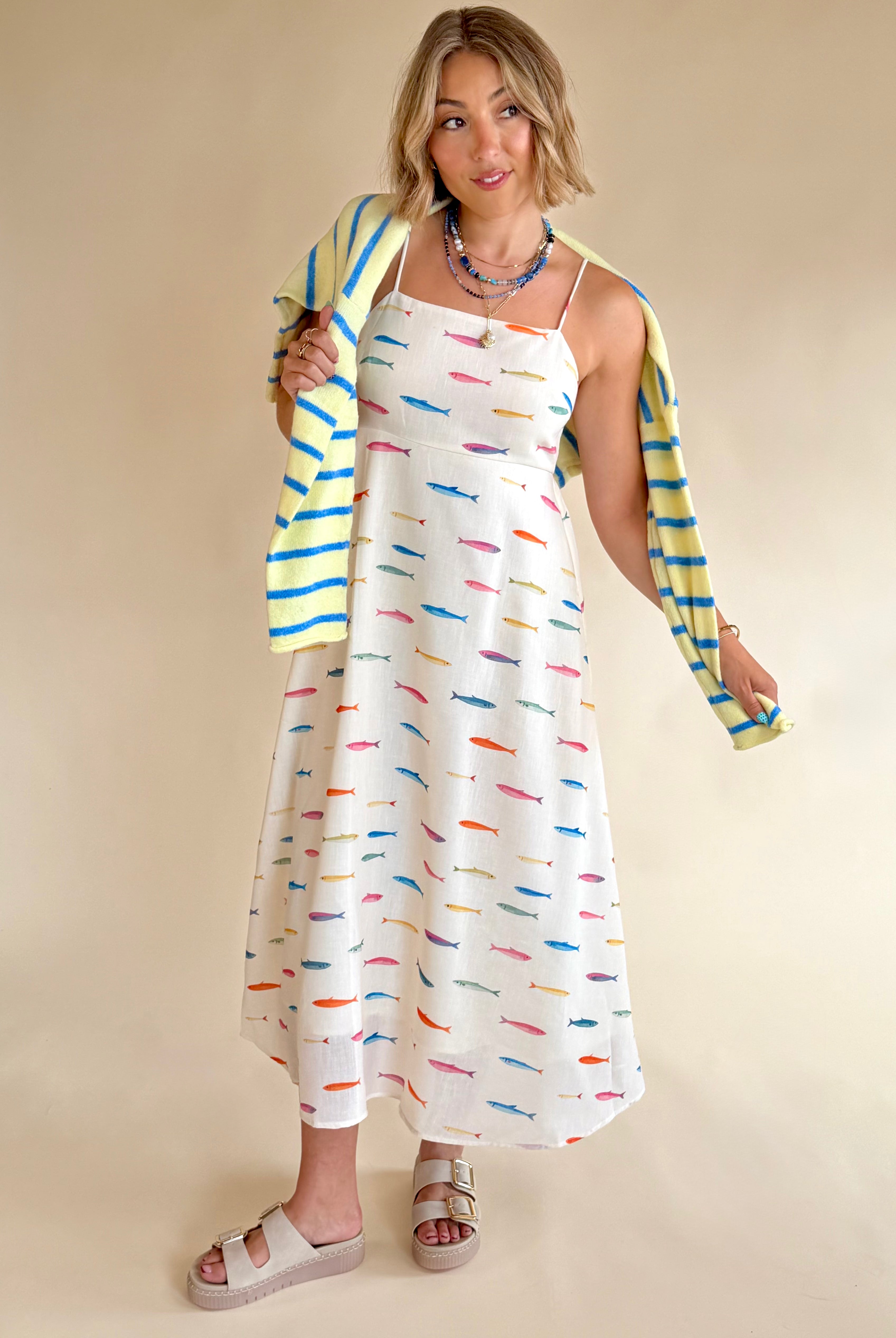 Woman wearing a colorful cardigan over a patterned dress on a beige background, maxi dress, spaghetti strap dress, rainbow, colorful, fish dress