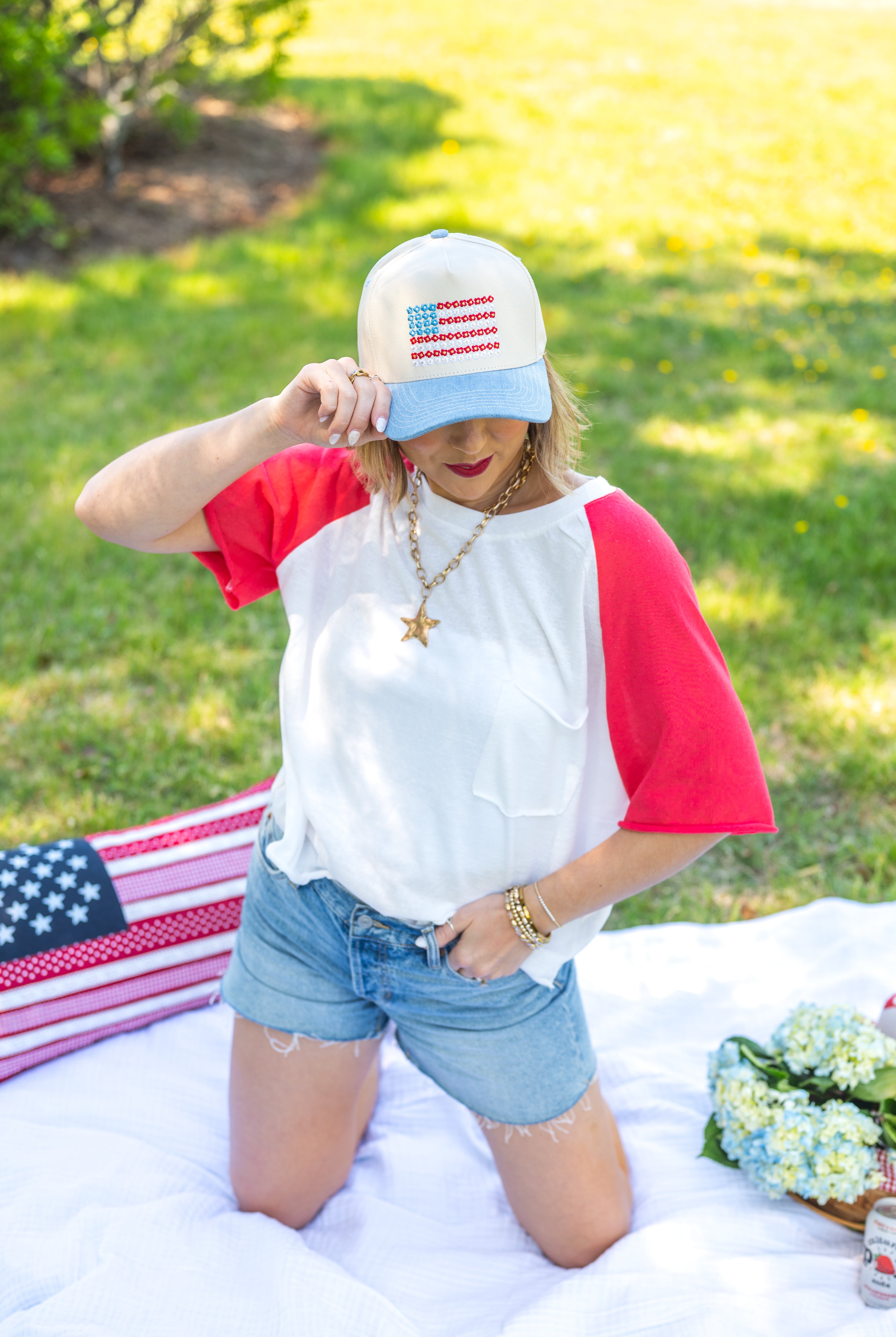 Woman in a red, white, and blue outfit with an American flag hat on a grassy outdoor setting, loose-fit tee shirt, red and white, USA, airy, breathable, pocket tee, raw hem , red sleeve