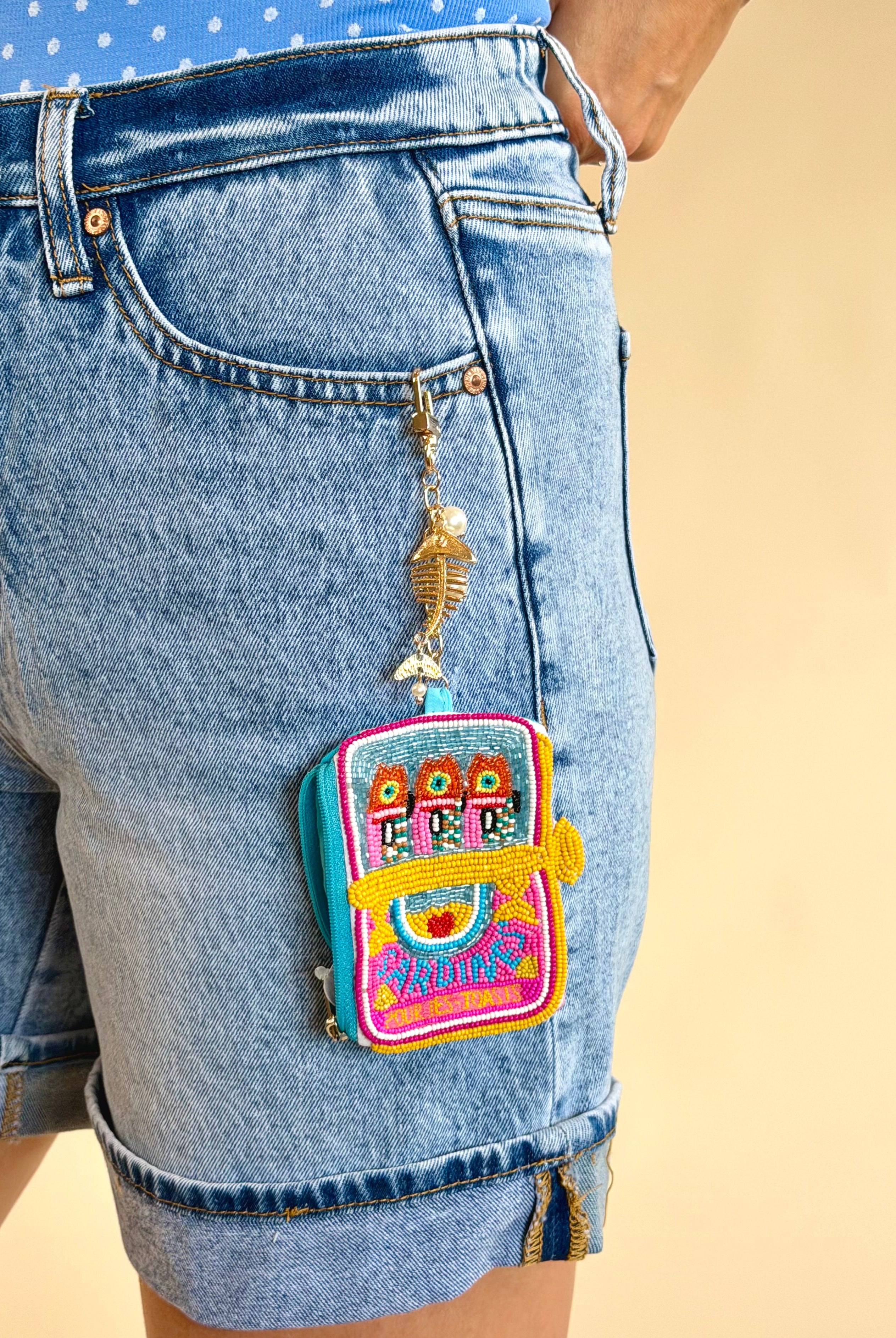 Colorful backpack charm on a denim shorts pocket against a beige background, sardine charm, mini wallet, keychain wallet, beaded detail, accessory, gifts