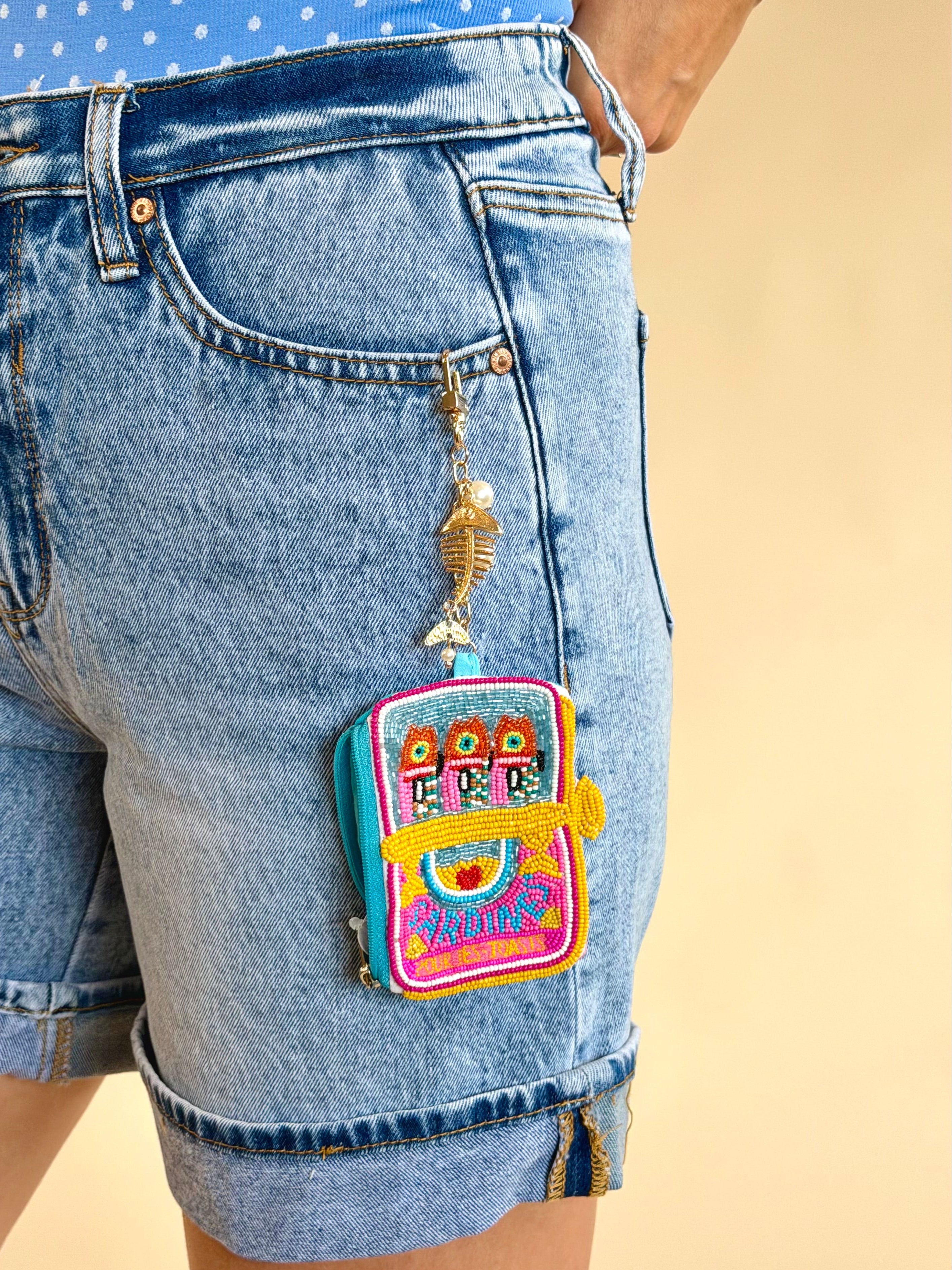 Colorful backpack charm on a denim shorts pocket against a beige background, sardine charm, mini wallet, keychain wallet, beaded detail, accessory, gifts
