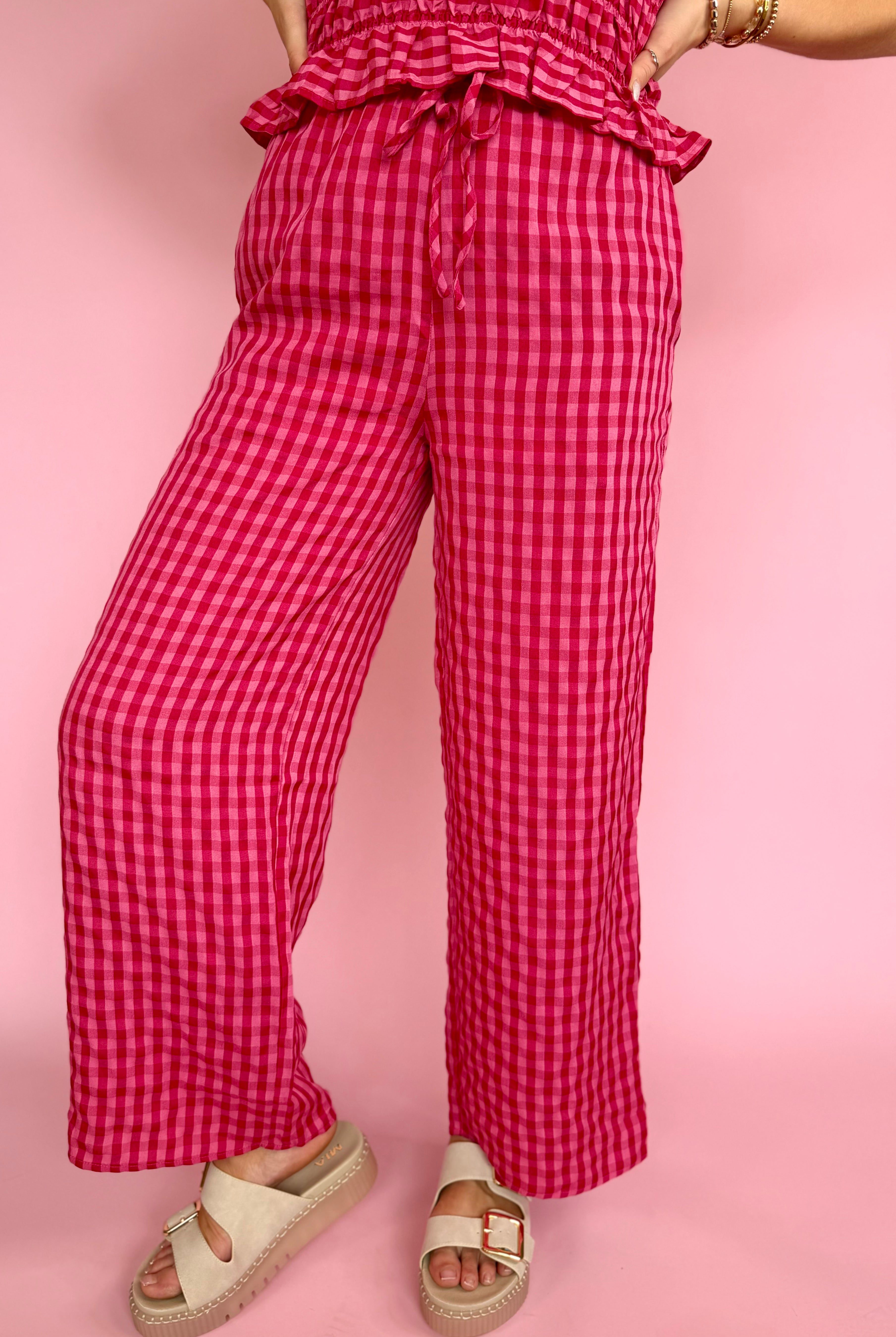 Person wearing red checkered pants on a pink background, draw string pant, wide leg lover, pink favorites, strawberry funk pant
