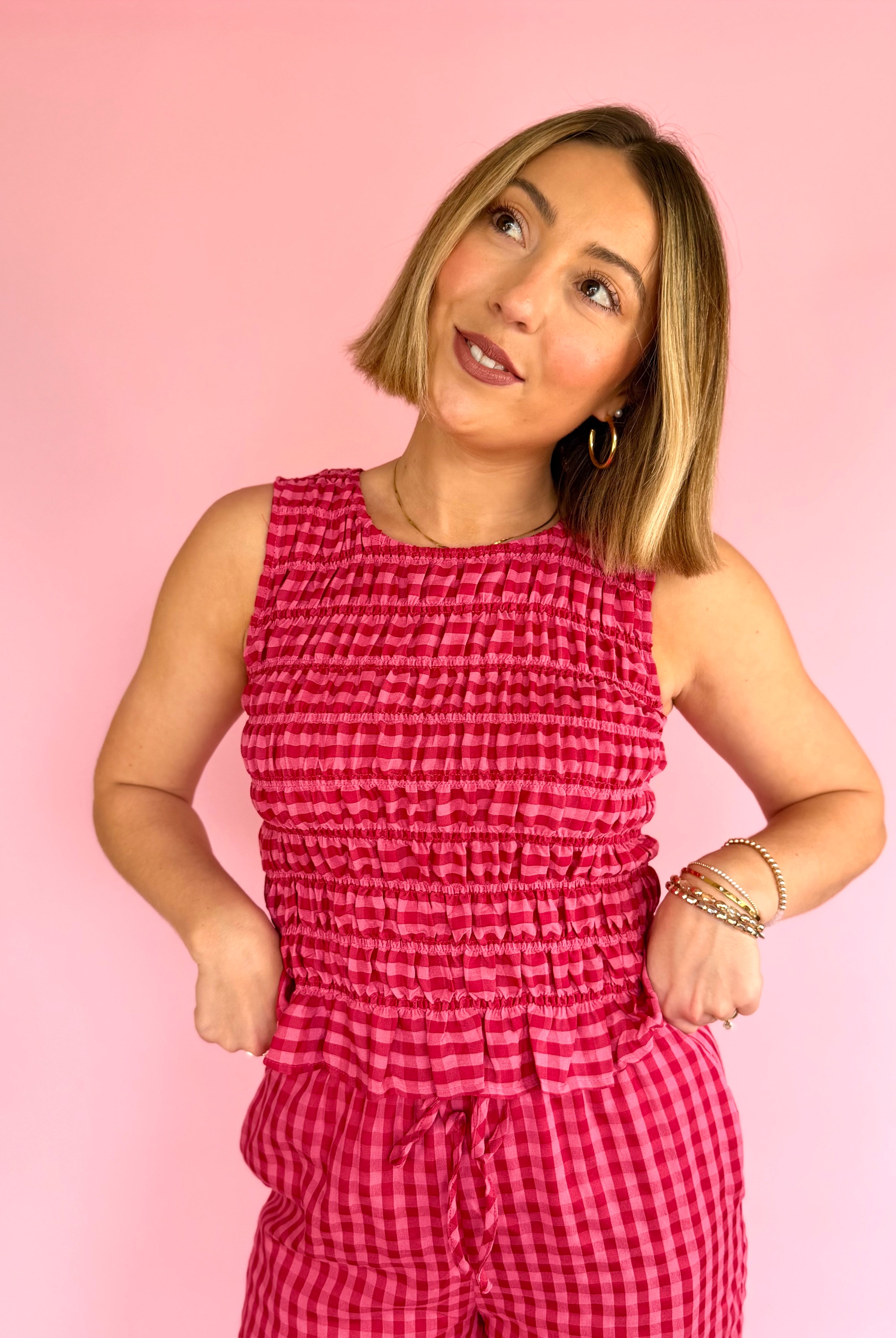 Woman wearing a pink checkered jumpsuit against a pink background, pink favorites, fitted smock tank, taste of strawberry, flared hem tank, full length summer tank
