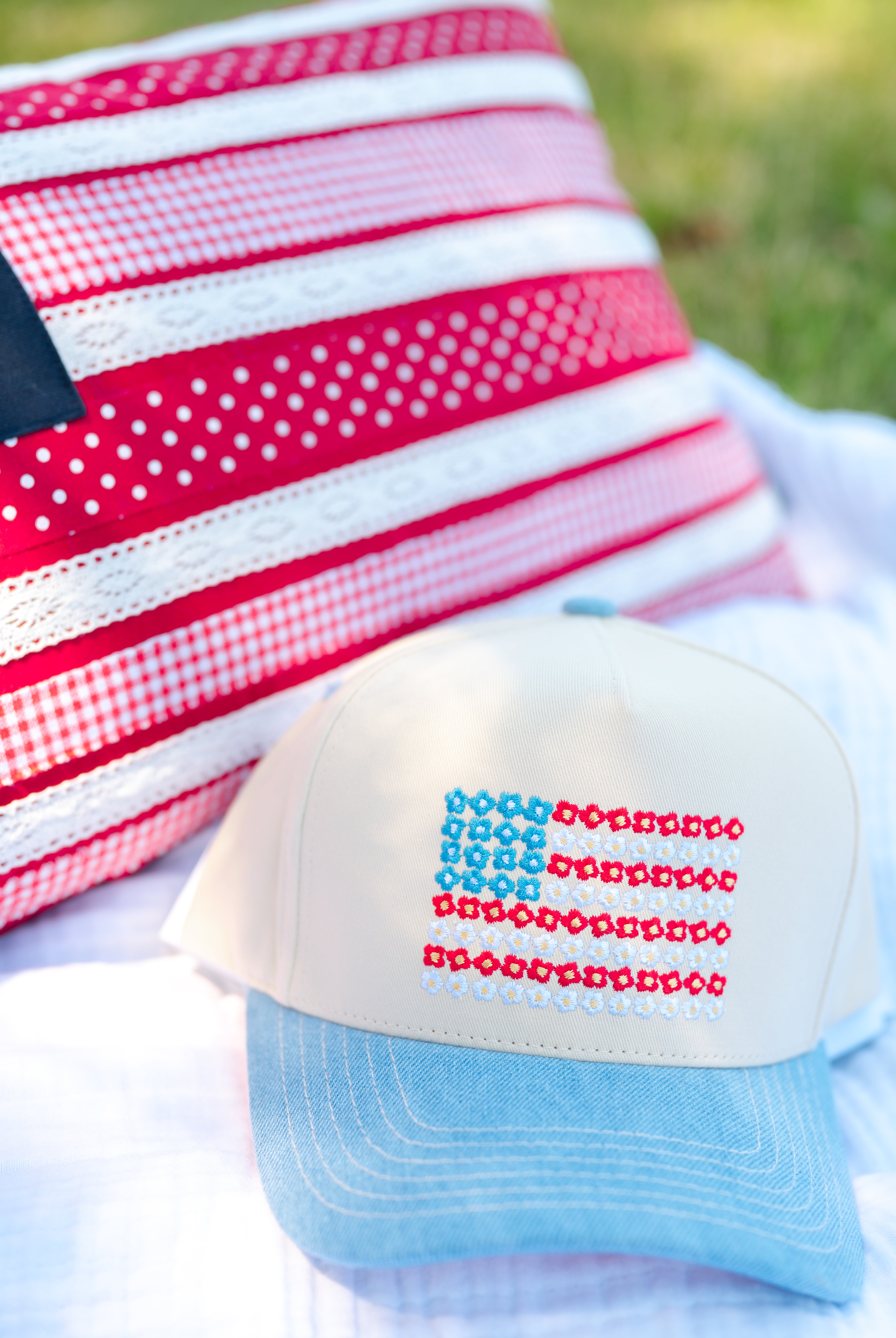Cap with American flag design on a white blanket with a red and white checkered fabric in the background, red white and blue, flower power, stars and stripes, denim hat