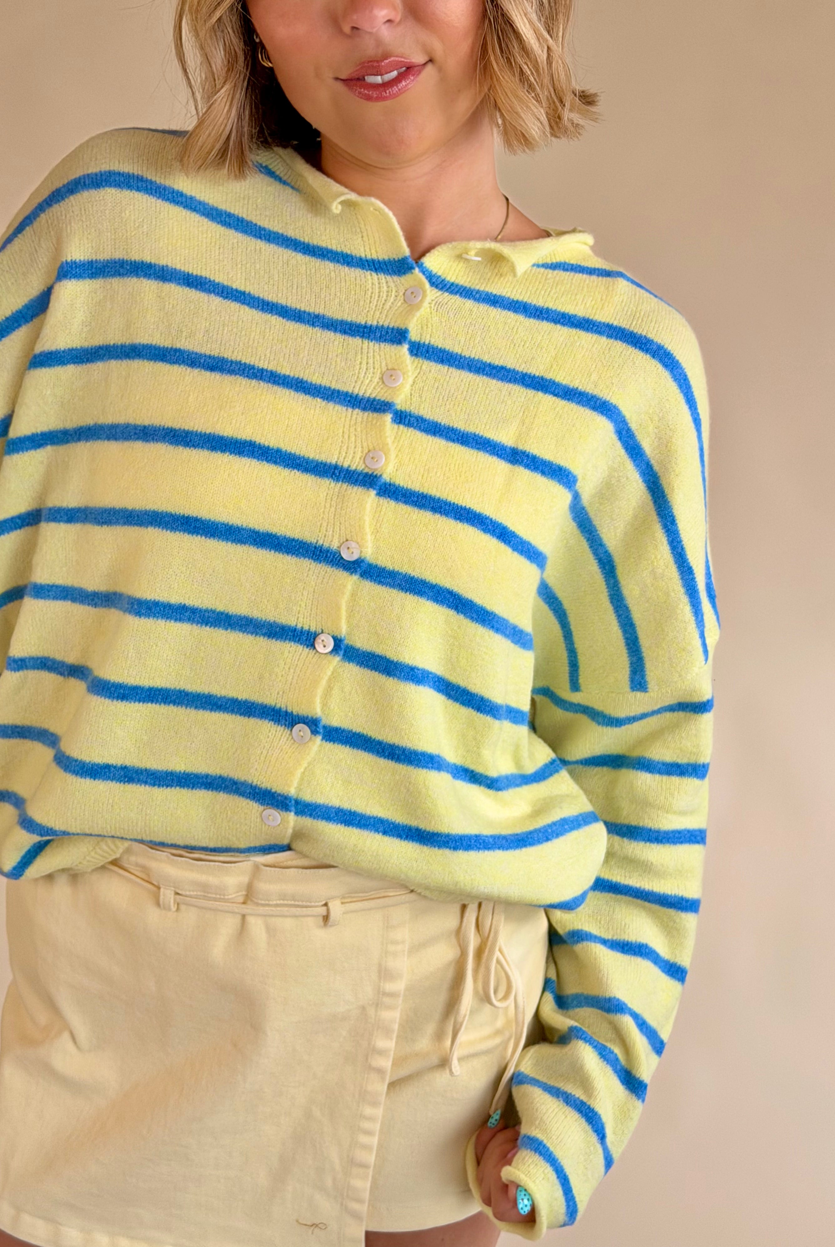 Person wearing a yellow and blue striped sweater against a beige background, yellow and blue sweater, button up sweater, stripe sweater, summer sweater