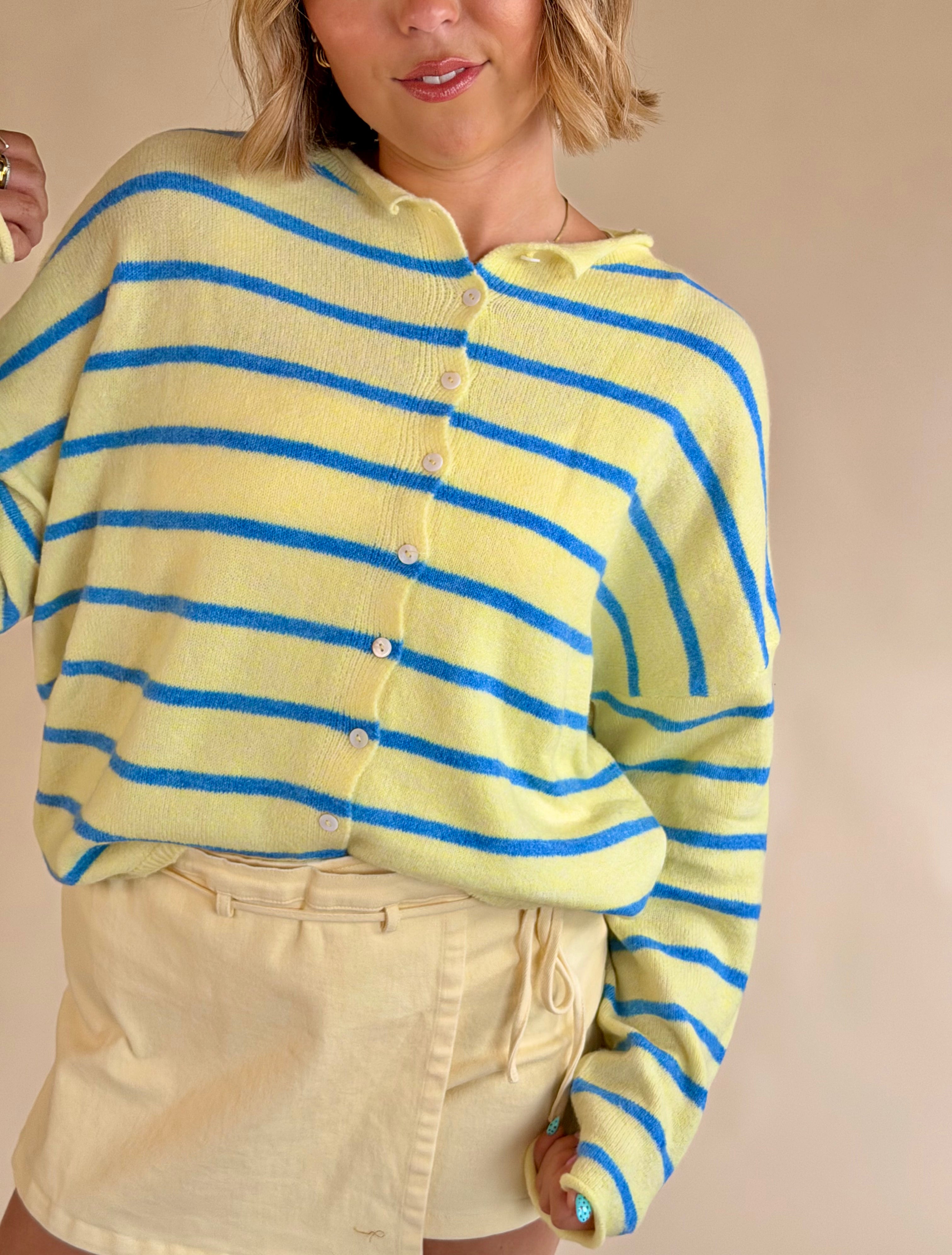 Person wearing a yellow and blue striped sweater against a beige background, yellow and blue sweater, button up sweater, stripe sweater, summer sweater