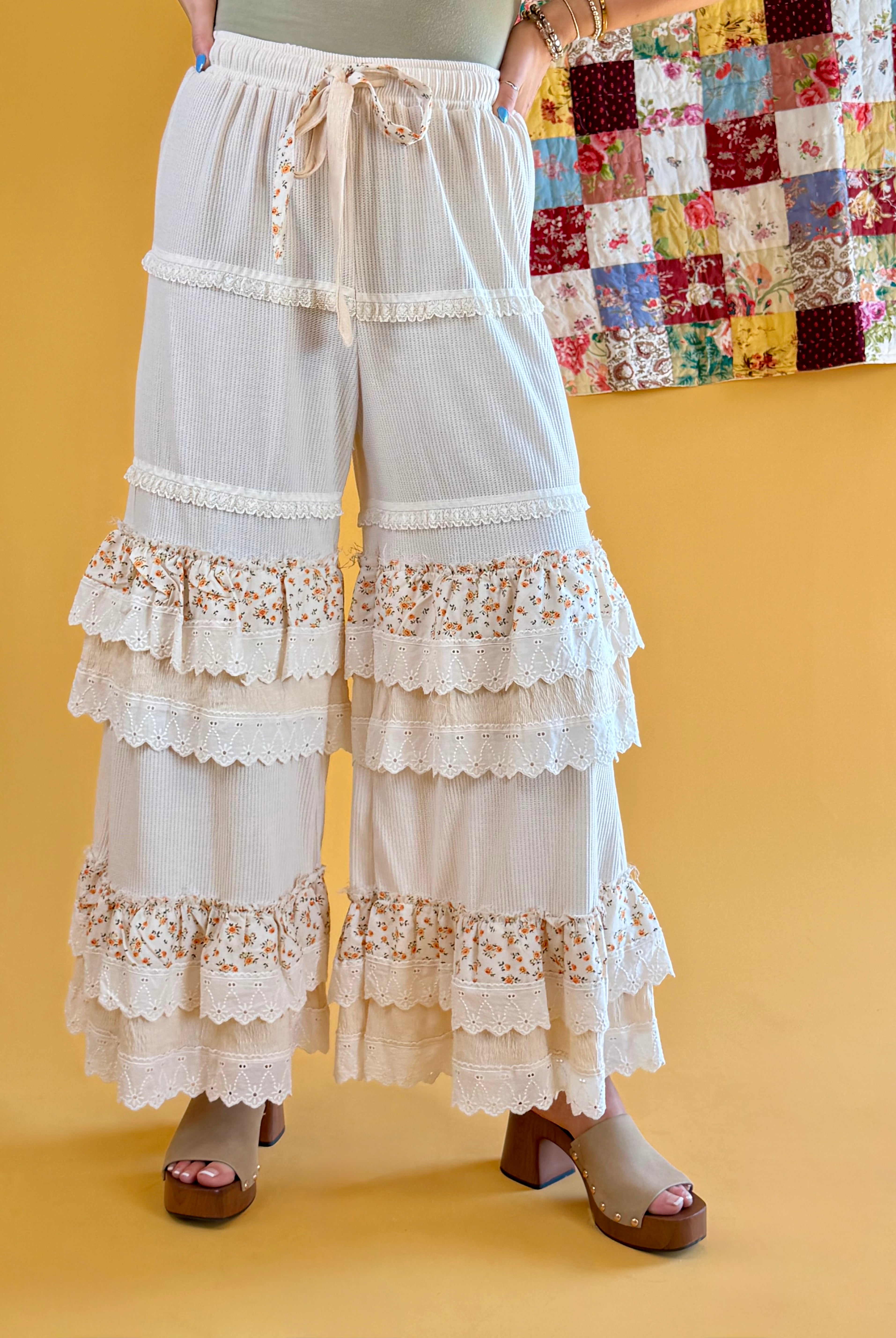White tiered lace pants with floral trim worn by a person on a yellow background, boho pants, beachy, floral wide leg, ruffles, lace, tall girl friendly