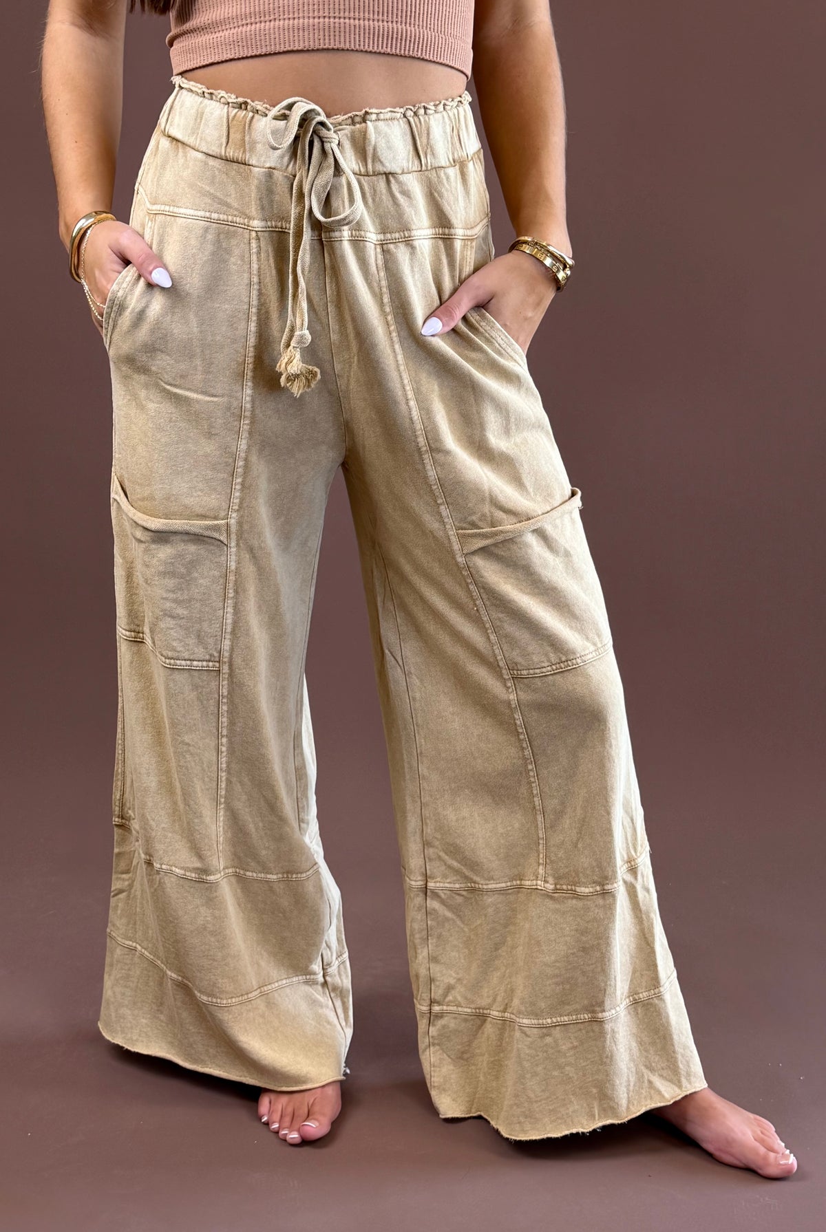 Camel Mist women’s mineral-wash pants with a relaxed wide-leg silhouette, elastic drawstring waist, roomy pockets, and raw-edge hems