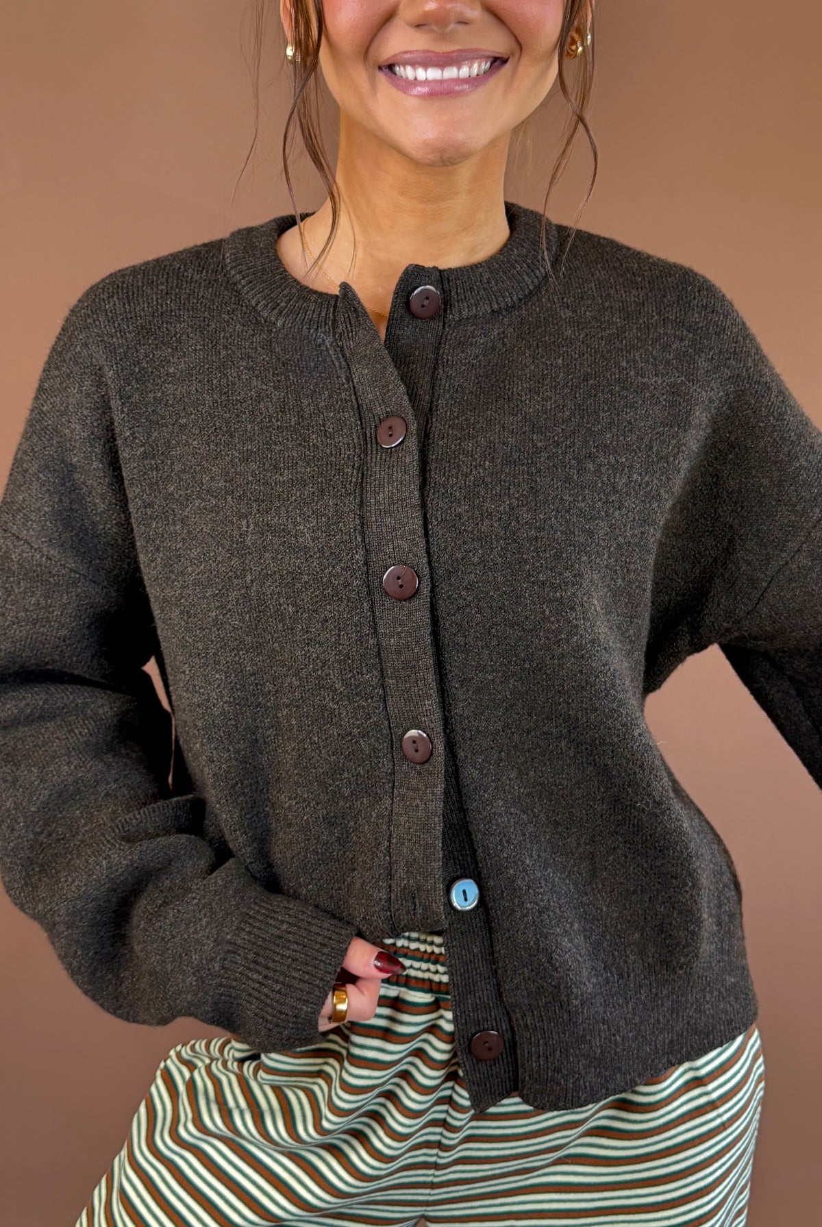 Model wearing a chocolate brown button-front cardigan with long sleeves and a round neckline, styled with striped pants.