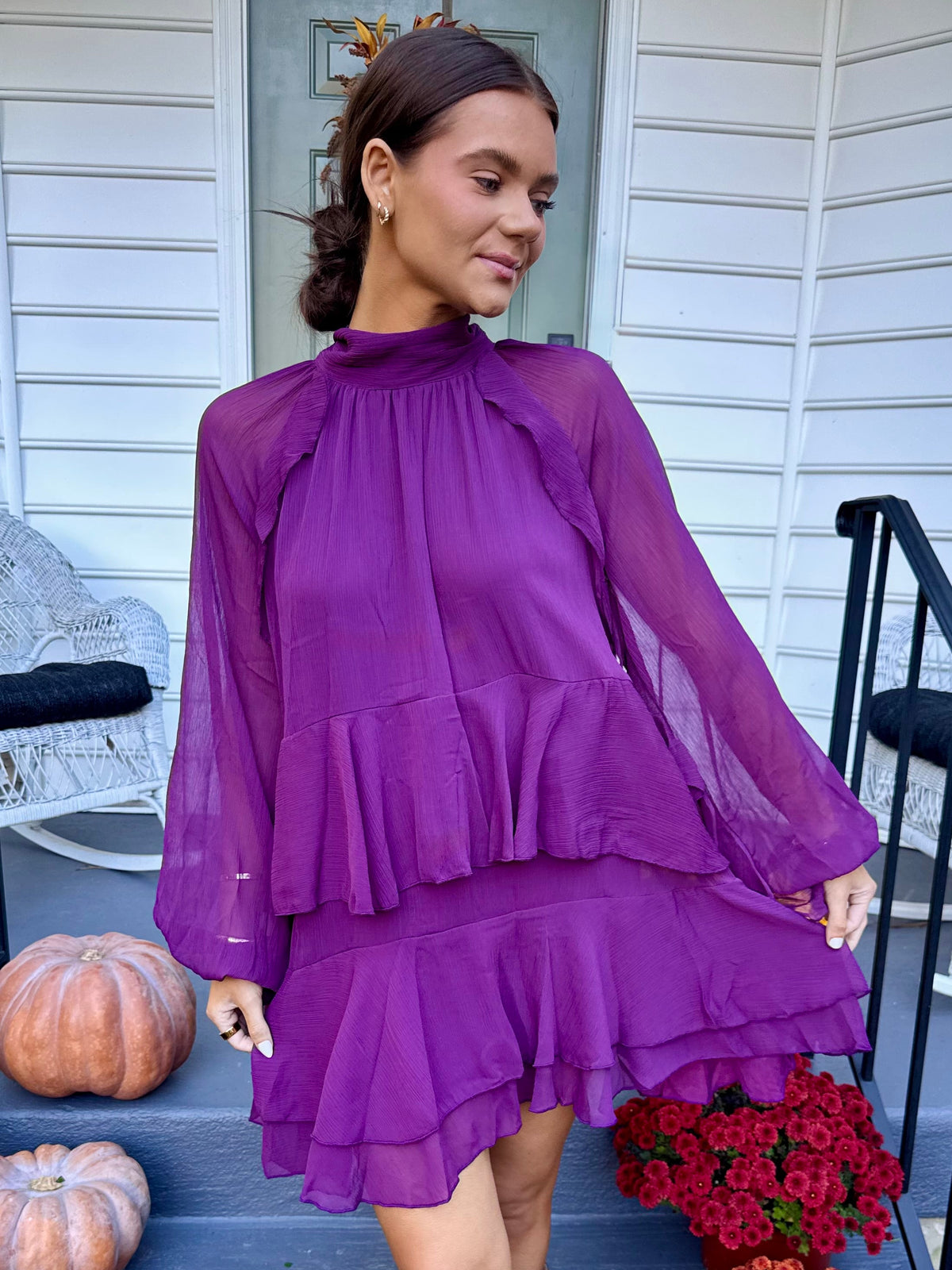 Model wearing the Friendsgiving ruffle mini dress in eggplant purple with a high neckline, long sleeves, a gathered waist, and a tiered ruffle mini hem.