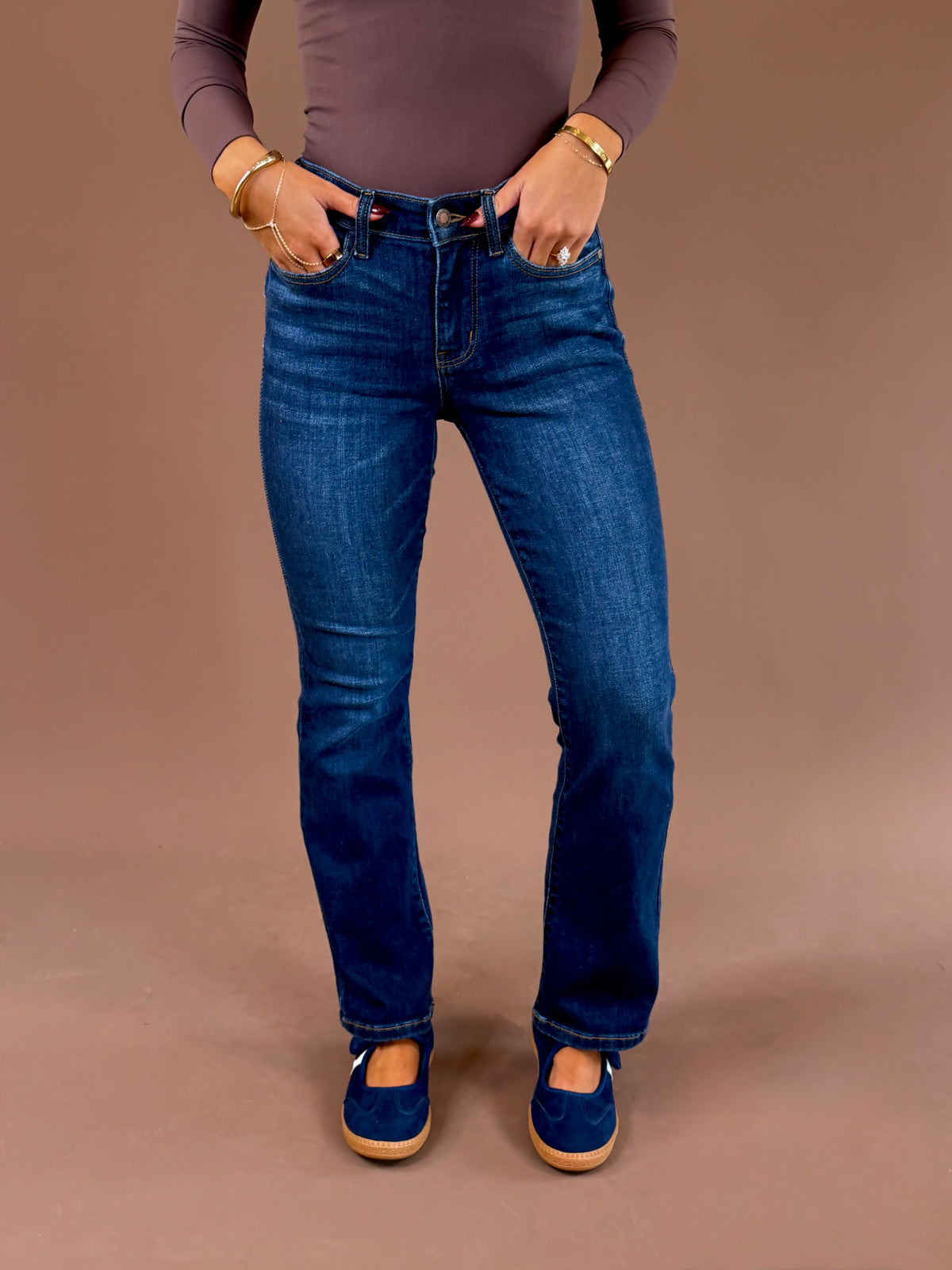 Front view of a model wearing Judy Blue dark wash mid-rise bootcut jeans with a 29-inch inseam, styled with a brown top and blue shoes.