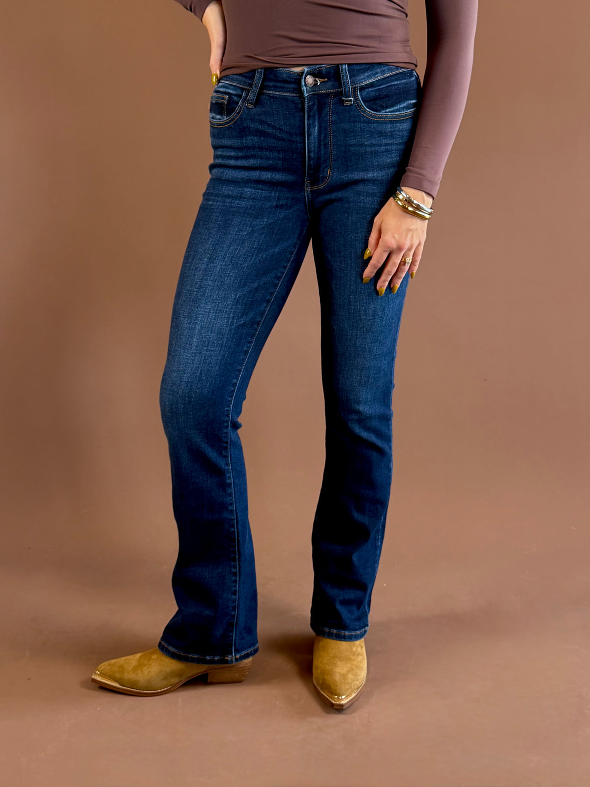 Front view of a model wearing Judy Blue dark wash mid-rise bootcut jeans with a 32-inch inseam, styled with a brown top and pointed-toe boots.