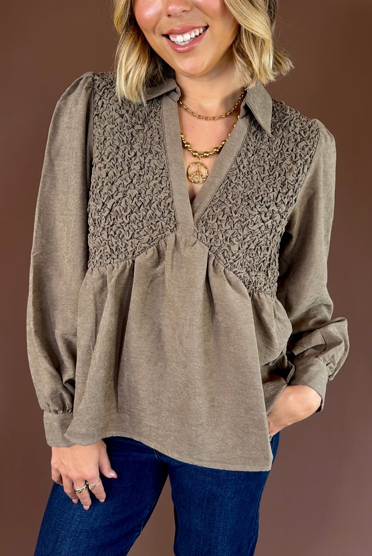 Taupe brown textured babydoll blouse with a collared V-neckline, long cuffed sleeves, and flowy fit.