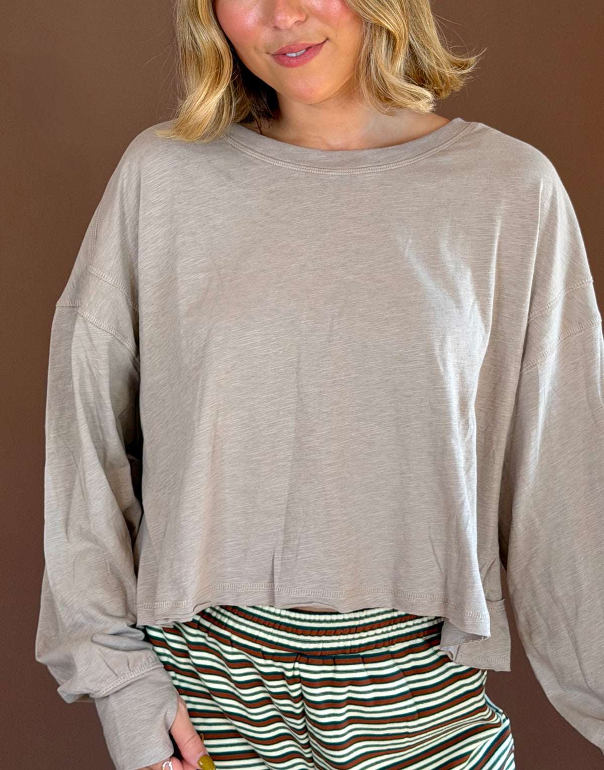 Model wearing a taupe relaxed long sleeve cotton top with a round neckline, styled with green striped pants.