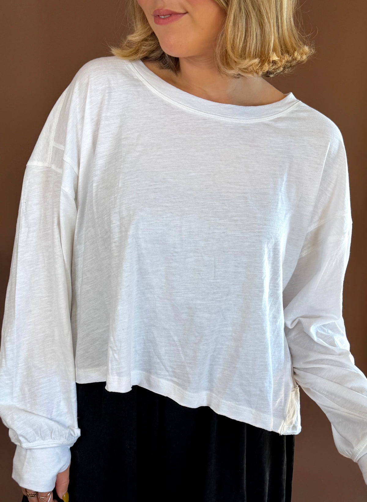 Model wearing a white relaxed long sleeve cotton top with a round neckline, styled with black pants.