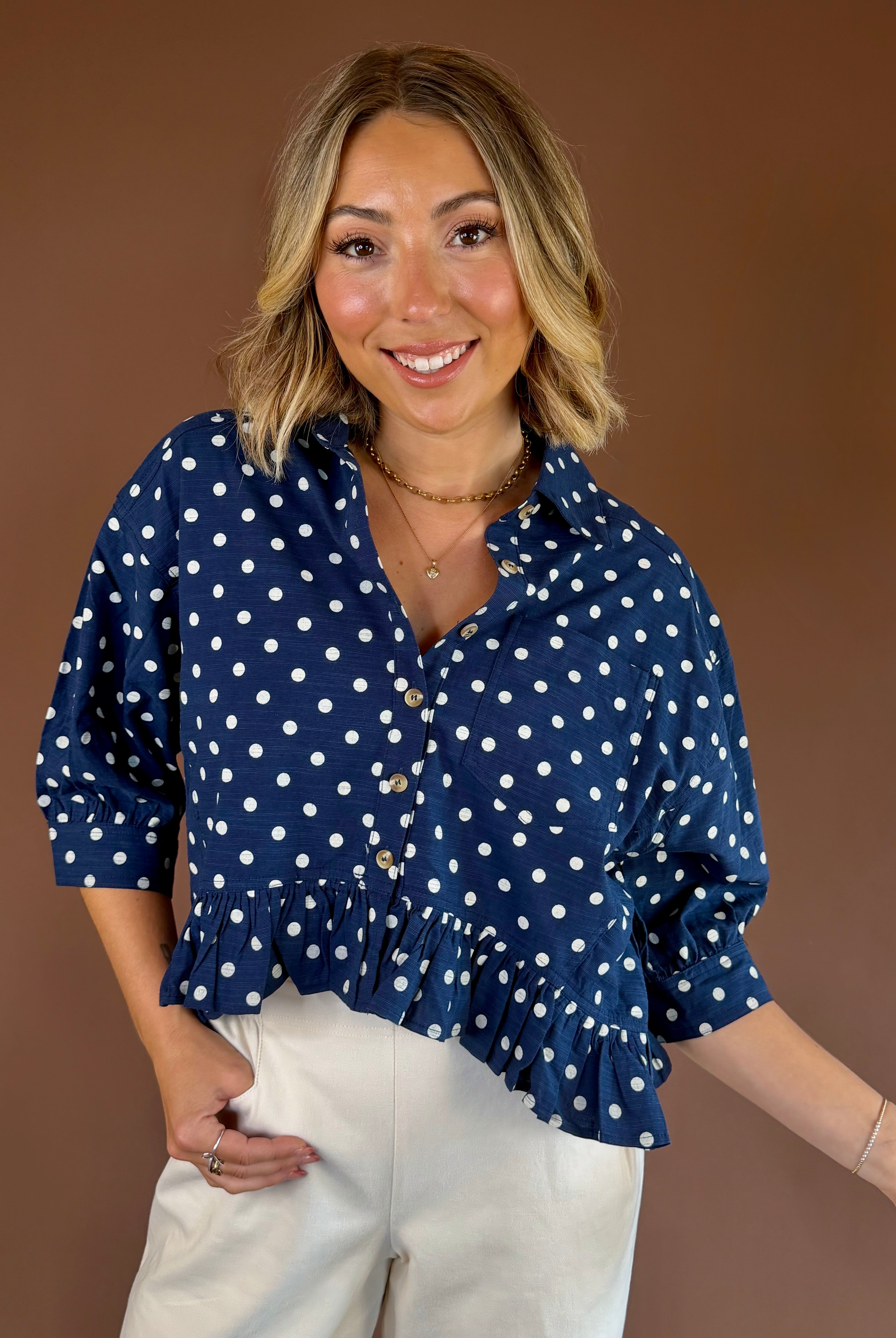 Navy blue polka dot button-down blouse with three-quarter sleeves, relaxed fit, and a ruffled hem.