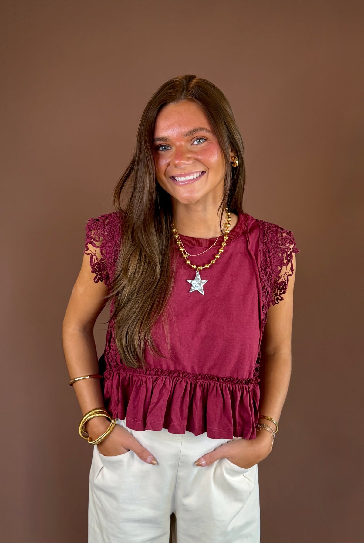 Wine-colored cotton top with a round neckline, cap sleeves, side lace trim, exposed seams, and ruffled hem.