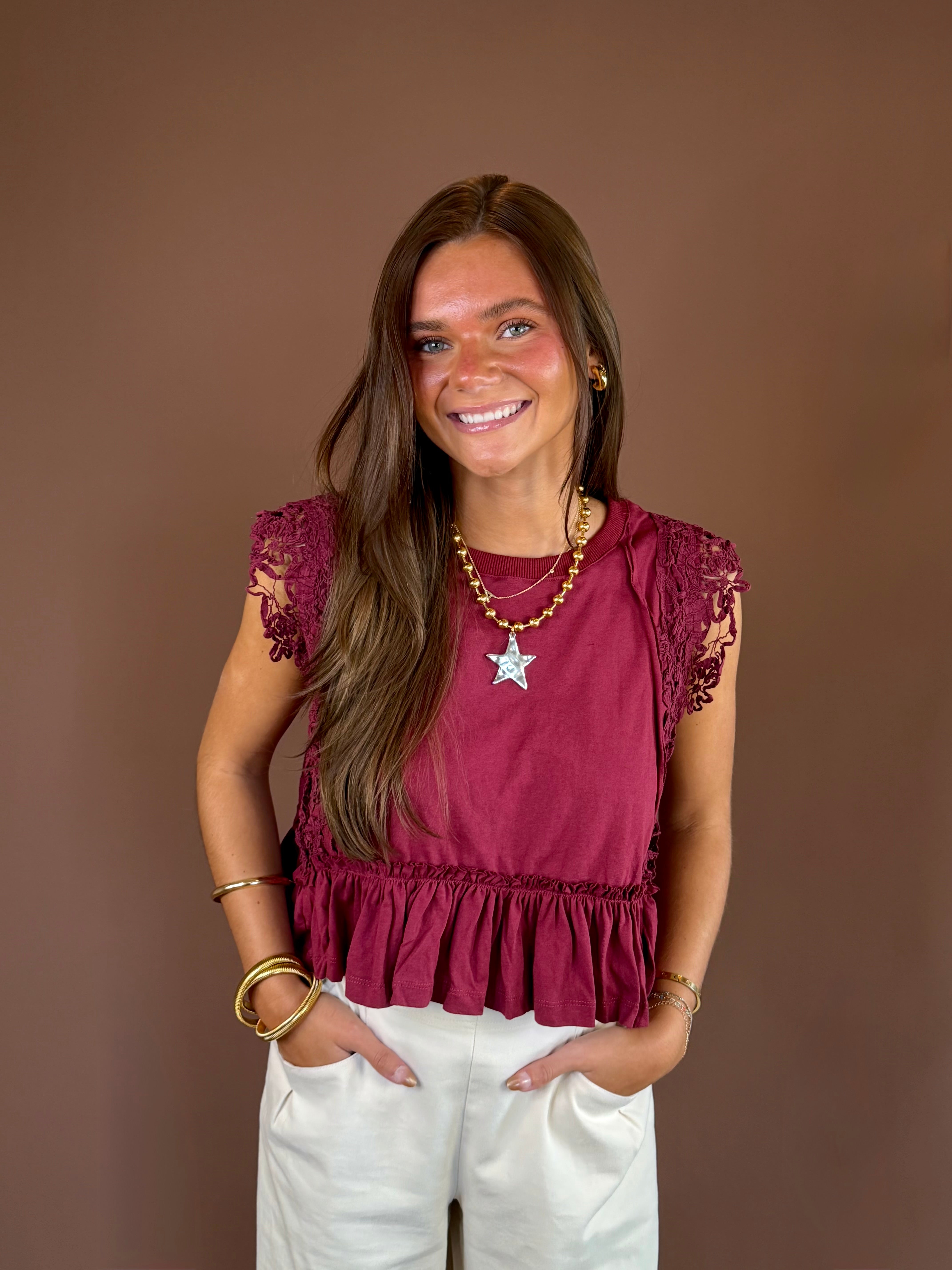 Wine-colored cotton top with a round neckline, cap sleeves, side lace trim, exposed seams, and ruffled hem.