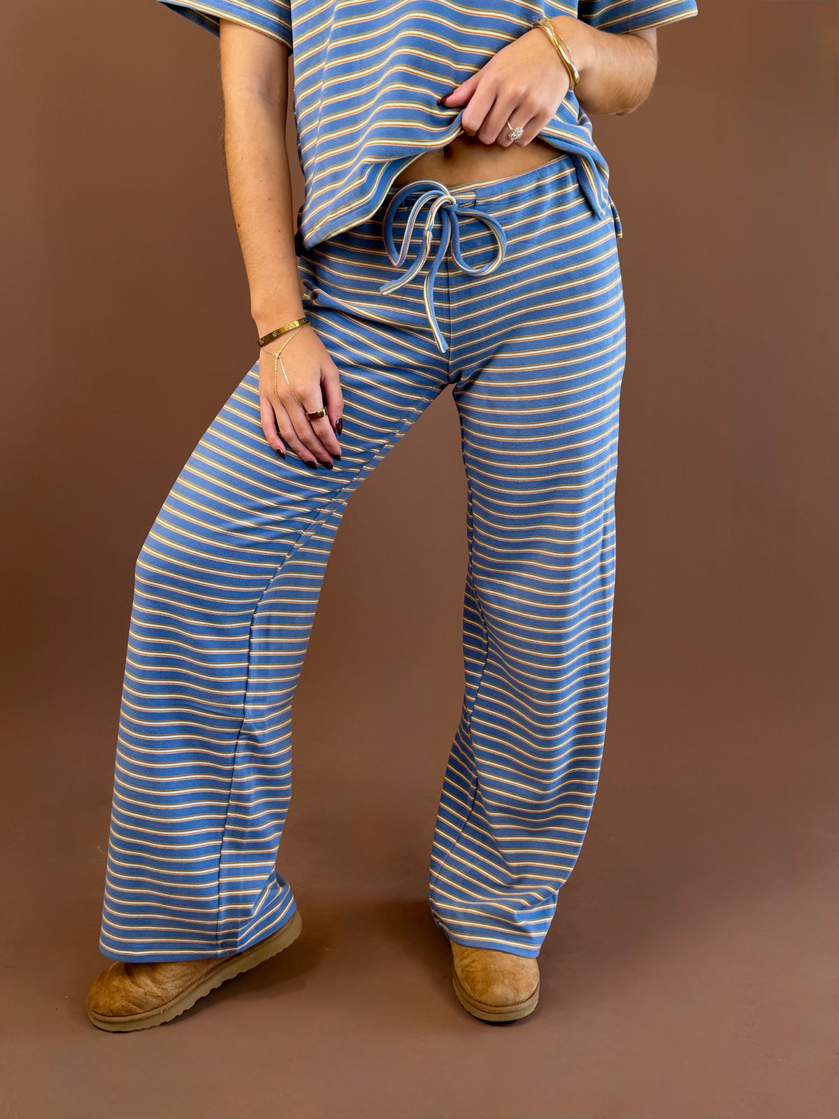 Model wearing dusty blue, yellow, and tan striped wide leg lounge pants with a drawstring waist and matching striped tee.