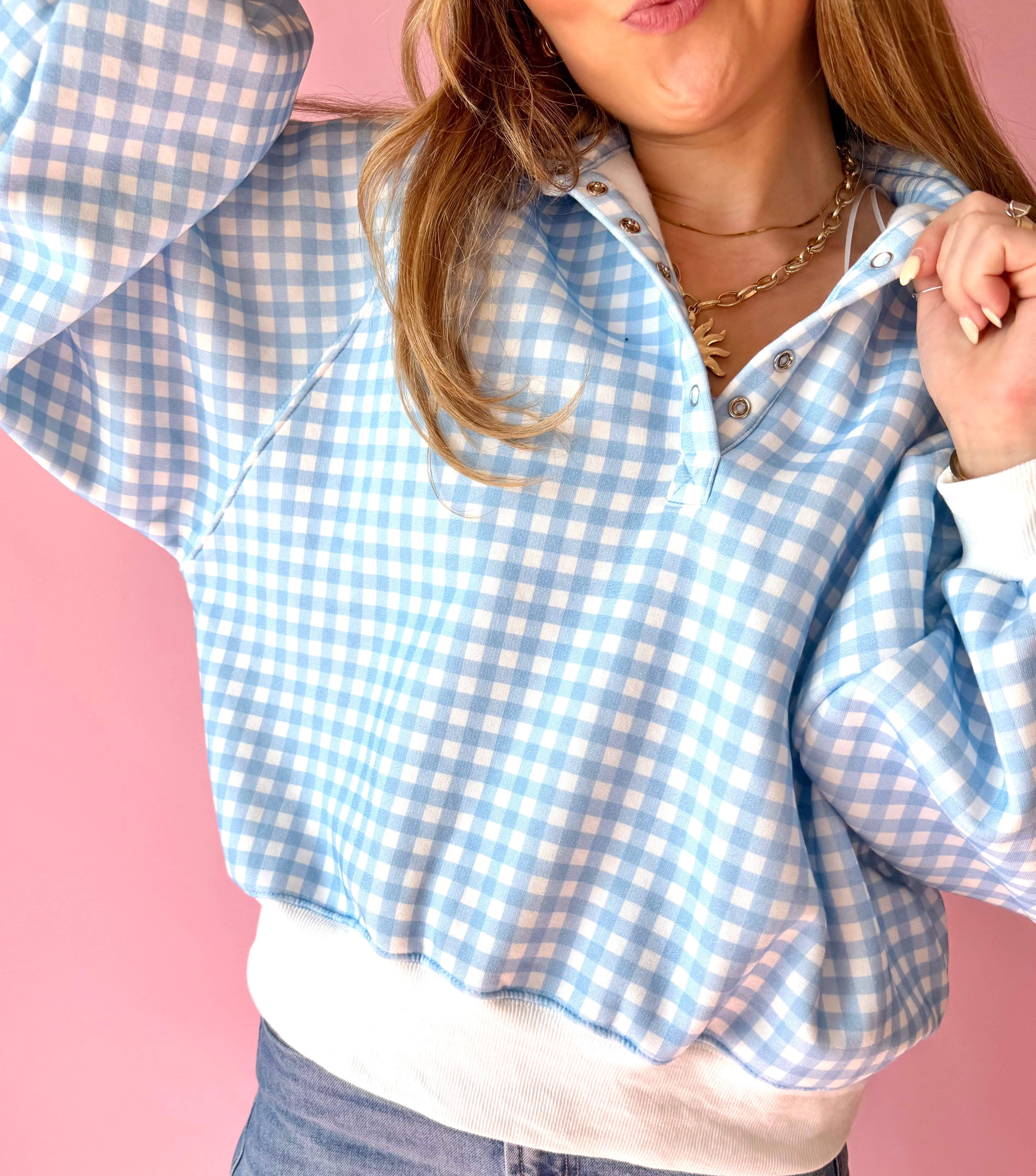 Person wearing a blue and white checkered shirt against a pink background, blue and white, gingham, blue picnic, quarter snap, over-sized, comfy pullover, lounge wear