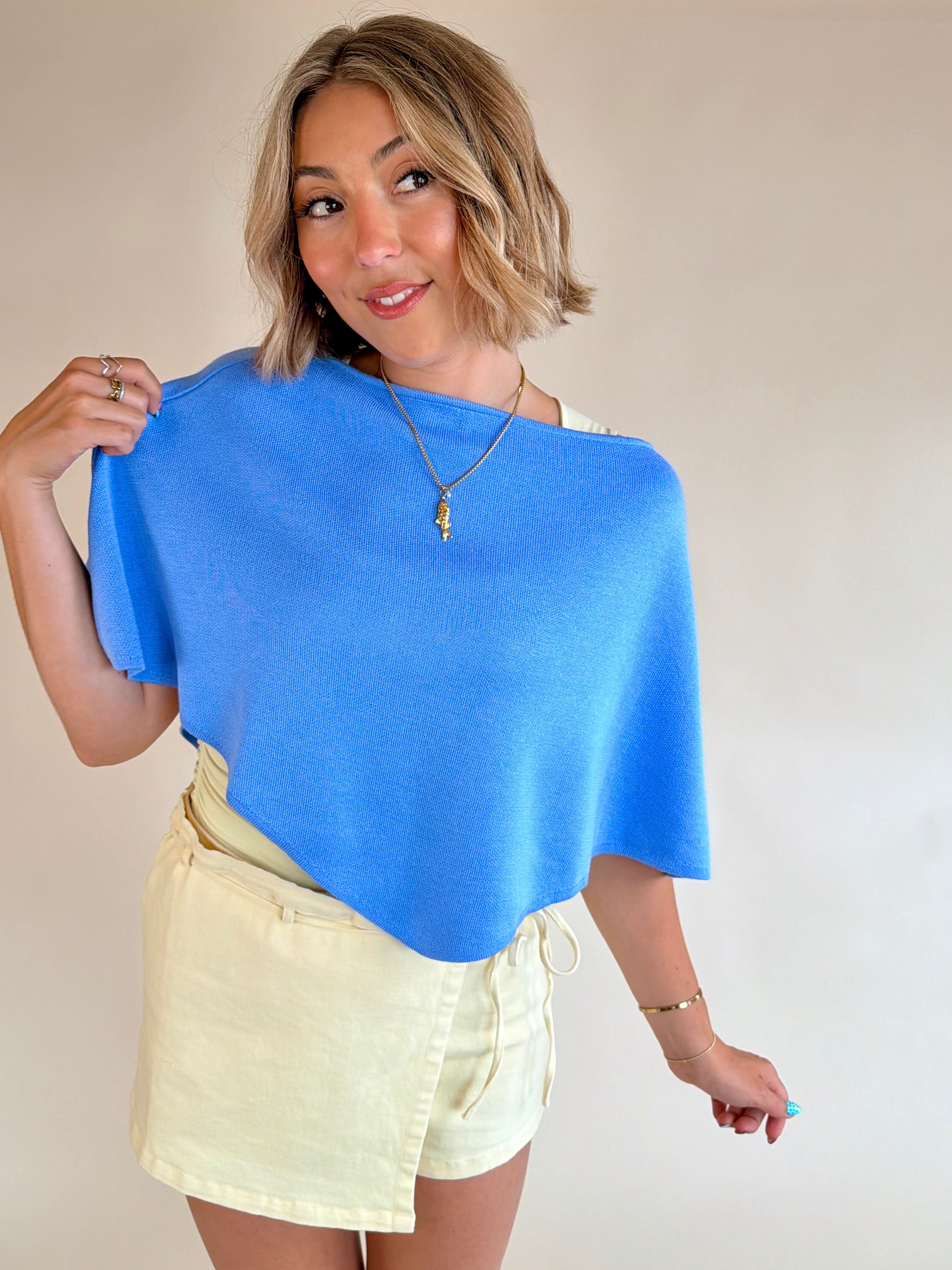 Woman wearing a blue top and yellow skirt against a plain background, Blue poncho top, summer staple, ocean blue, style piece, flattering fit 