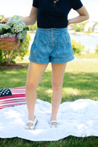 Person wearing denim shorts holding flowers on a grassy field with an American flag in the background, flared, button fly, summer essential