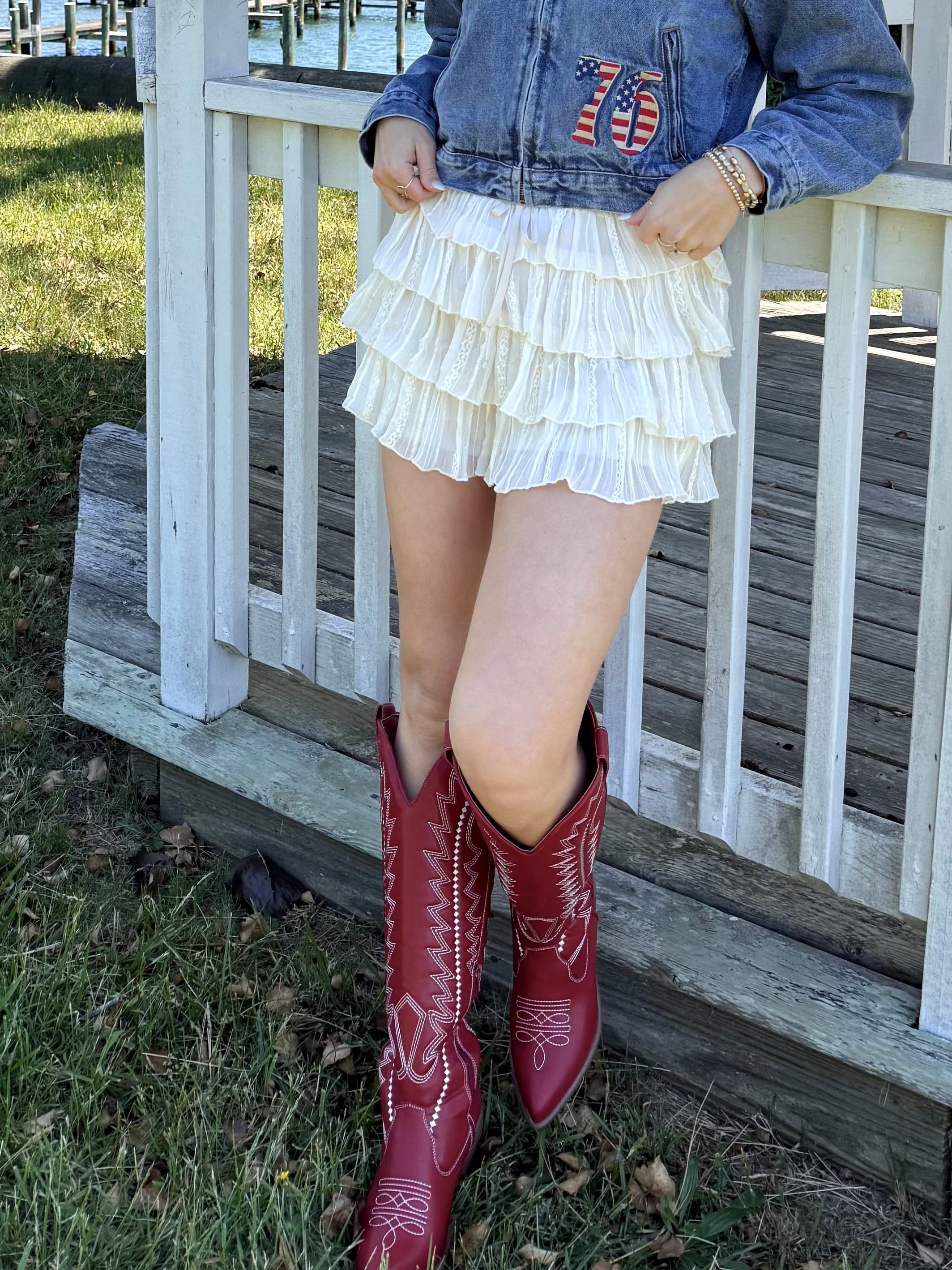 Woman in denim jacket and red boots standing on a porch by a lake, cream, airy, flowy, breathable, comfy, effortless, shimmer skirt, mini