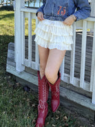 Woman in denim jacket and red boots standing on a porch by a lake, cream, airy, flowy, breathable, comfy, effortless, shimmer skirt, mini
