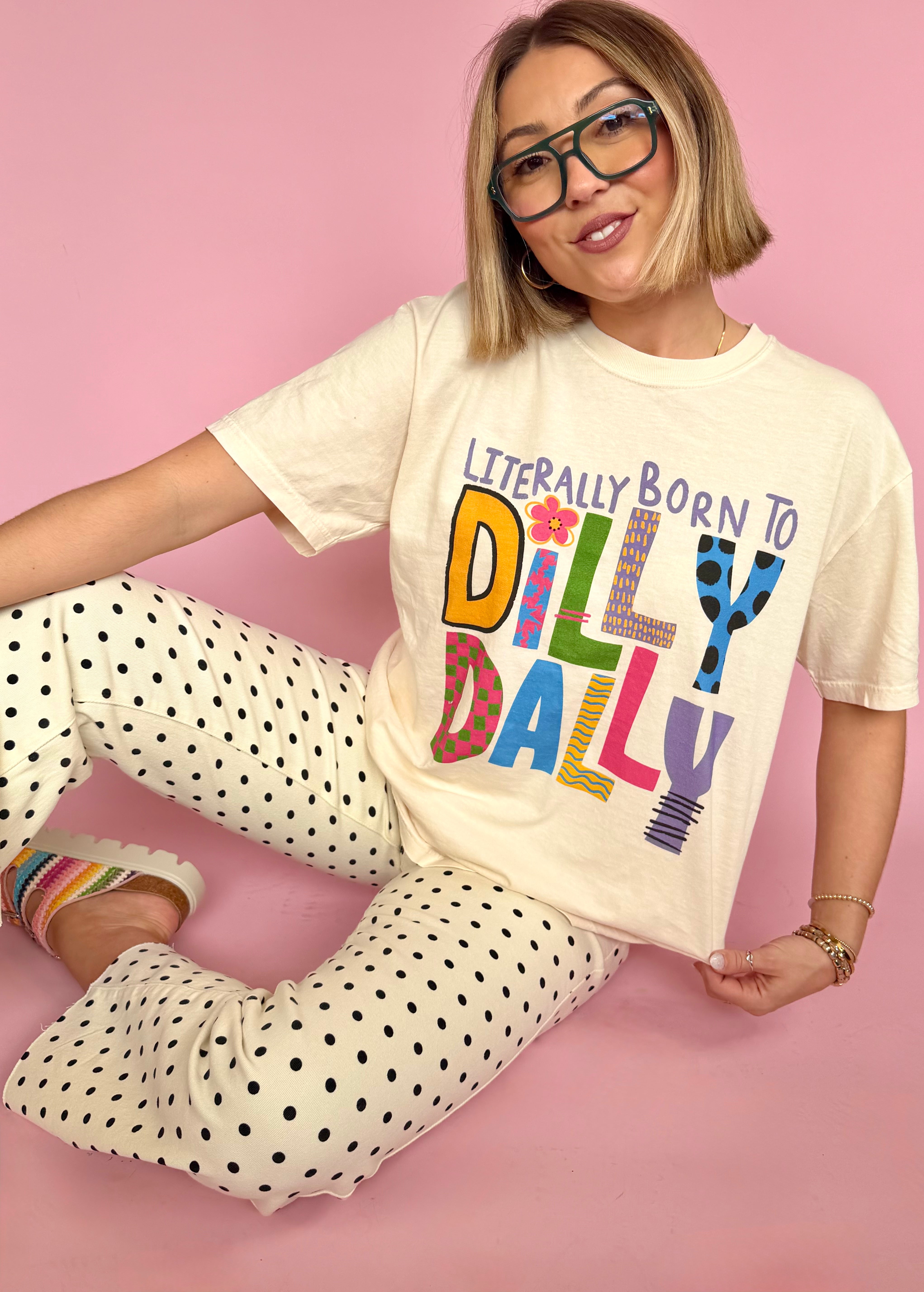 Person wearing a cream t-shirt with colorful text and polka dot pants on a pink background, pattern lovers perfect tee, comfortable, everyday wear