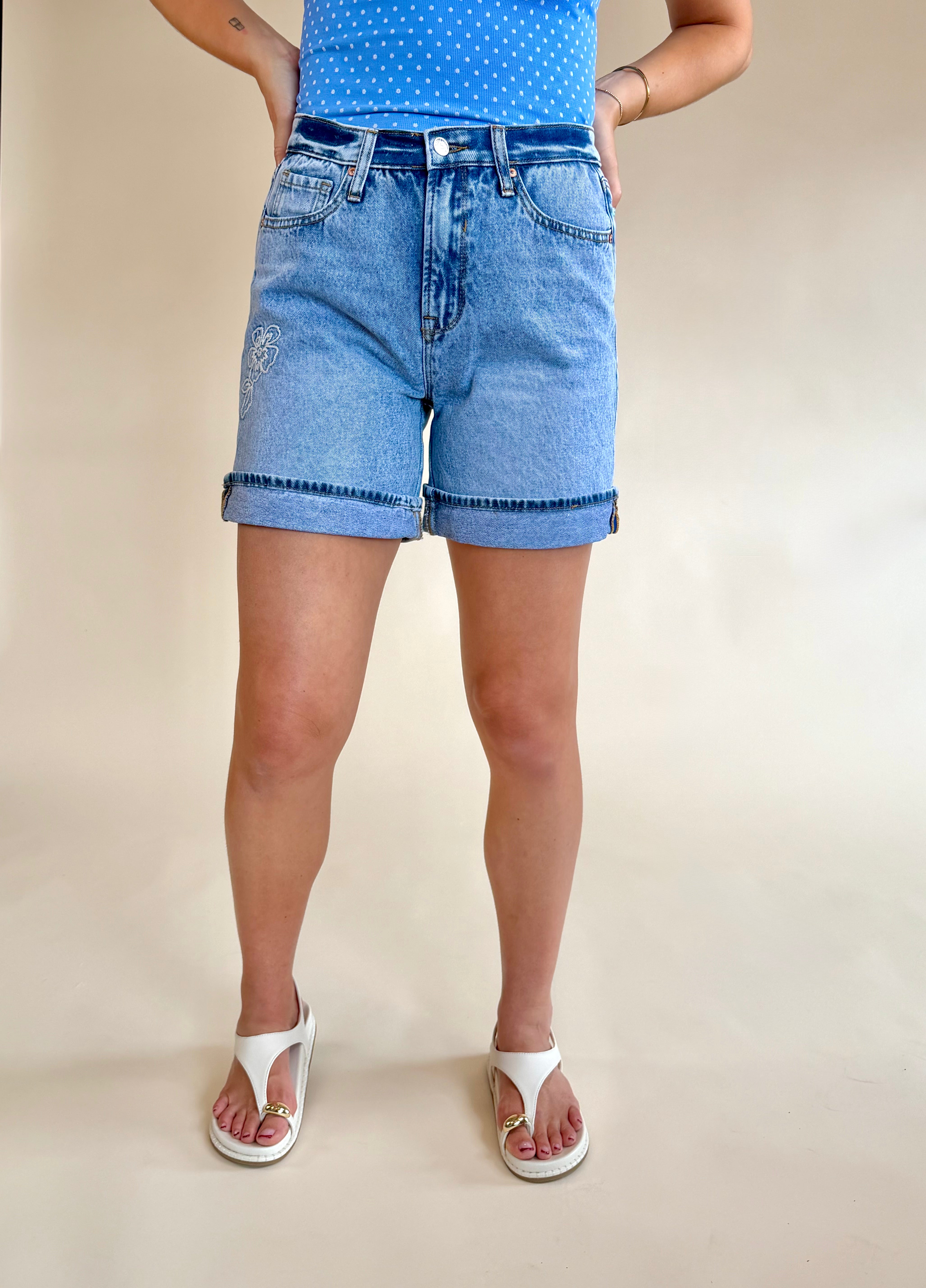 Person wearing blue denim shorts on a beige background, flower detail, foldover denim short, summer staple, everyday wear, blue flower denim