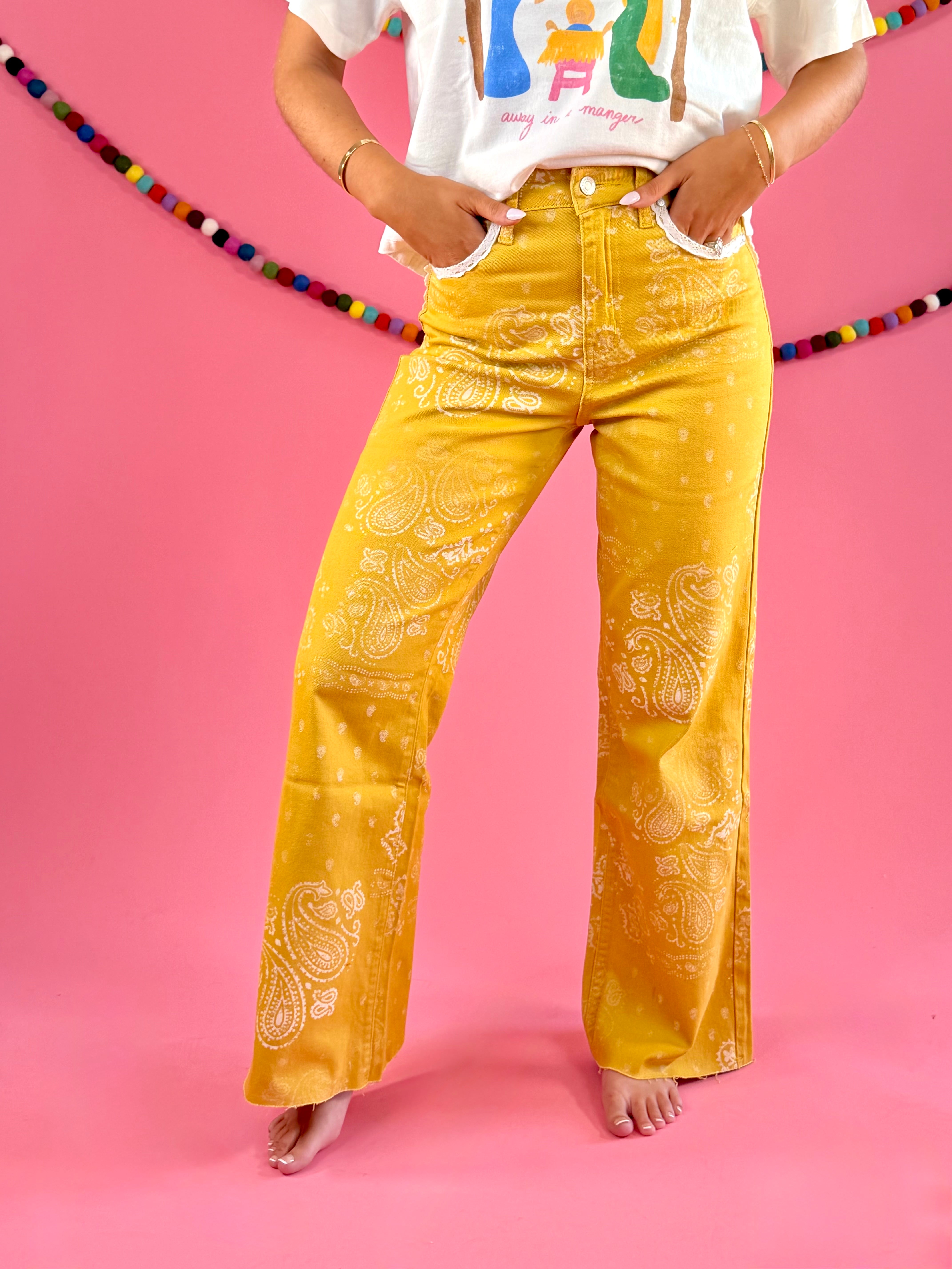 Front view styled with ivory graphic tee: POPPY & PINE mustard yellow bandana paisley denim pants with frayed hems.