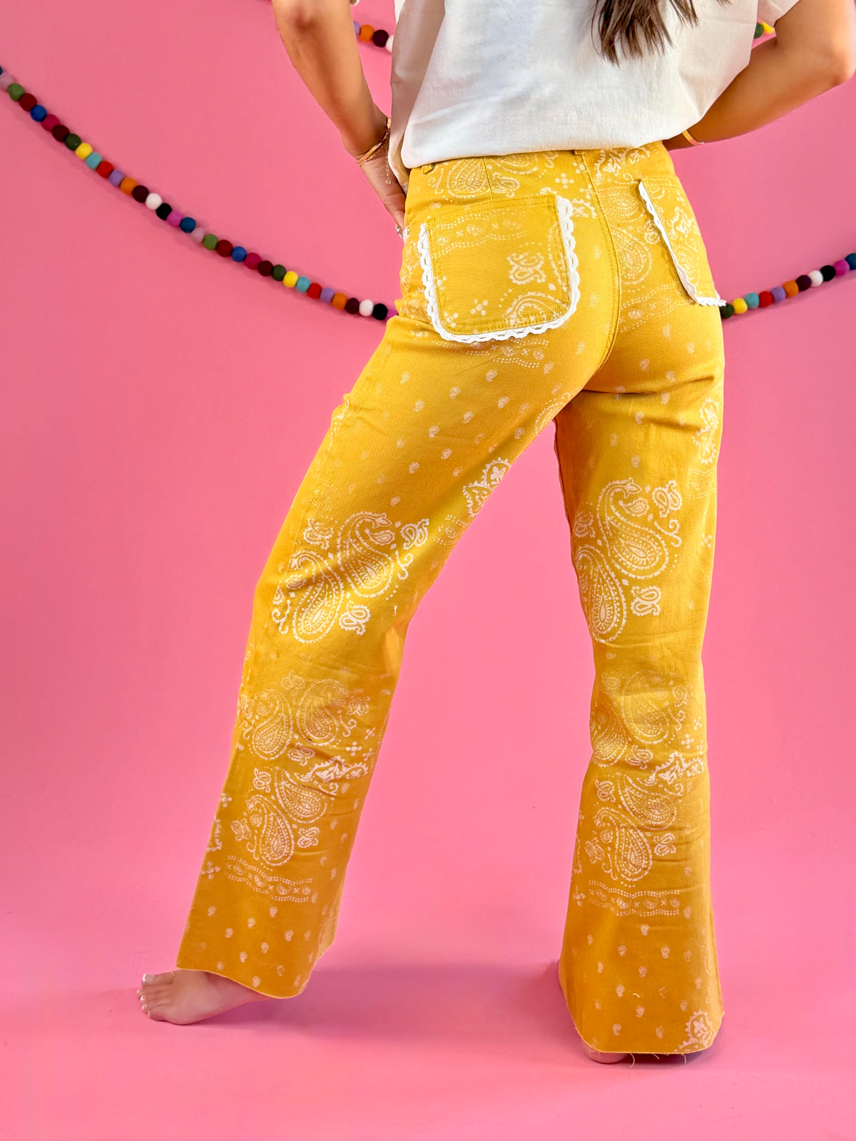 Side and back fit view: POPPY & PINE mustard yellow bandana paisley denim pants with frayed hems.