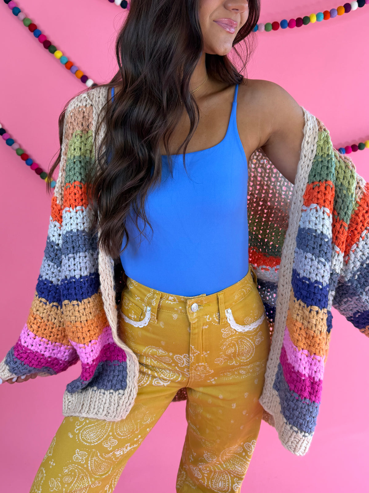Styled with blue tank and mustard pants: Cream Rainbow Cardigan with multicolor stripes, an open front, and hip pockets.