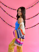 Side view: Cream Rainbow Cardigan with multicolor stripes, an open front, and hip pockets.