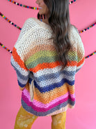 Back view: Cream Rainbow Cardigan with multicolor stripes, an open front, and hip pockets.