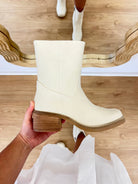 White boot held in a hand with a wooden floor background, TRENDY BOOT, it girl boot, bootie, boho style, coastal, bone