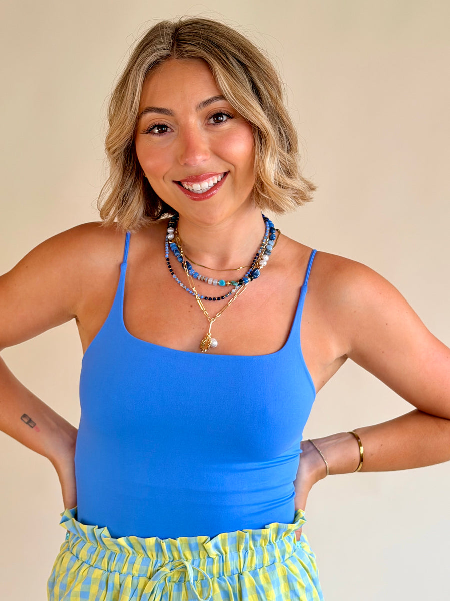Woman wearing a blue tank top and yellow plaid shorts with a beige background, everyday basic, blue tank, flattering fit, marina blue 