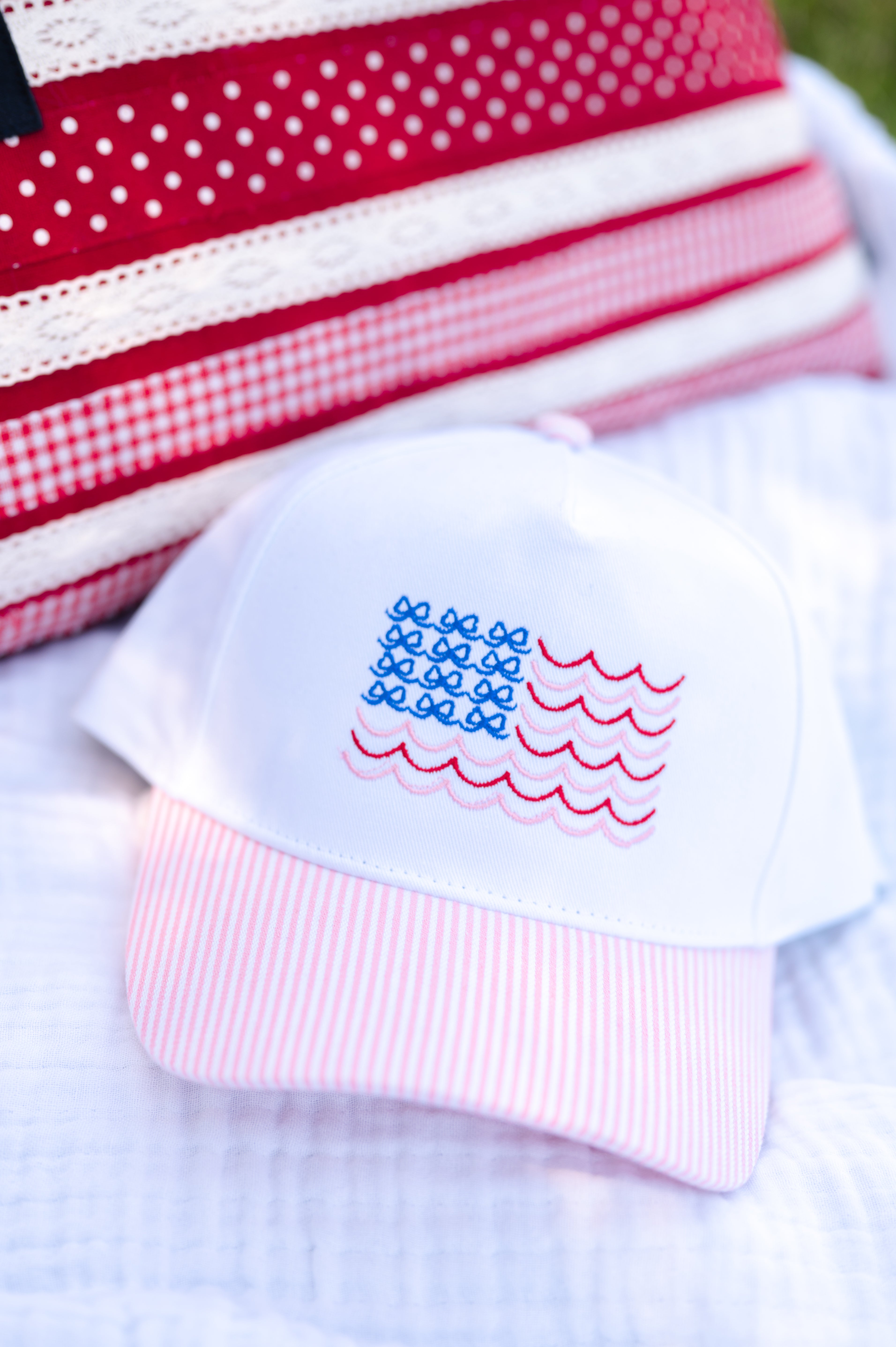 White baby hat with American flag design on a white blanket, pink and white, bows and stripes, beachy and bows, USA